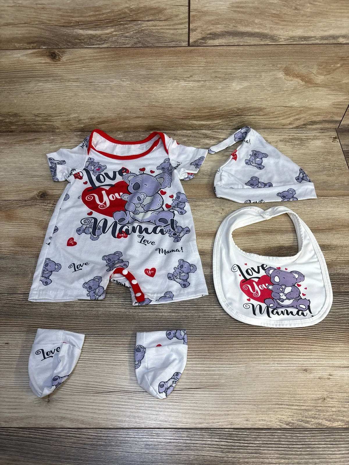 Baby romper outfit set with koala bear print, matching hat, mittens, and bib on wood floor