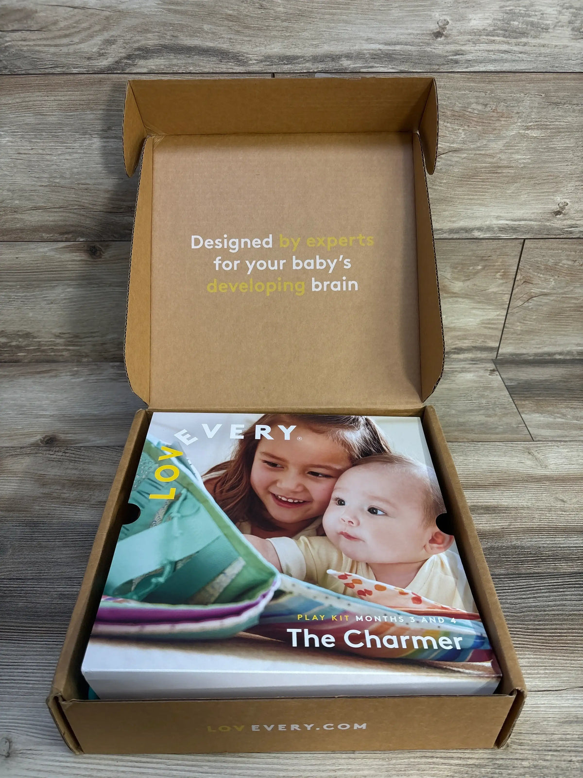 Top view of Lovevery The Charmer Play Kit in open box with text Designed by experts for your baby’s developing brain