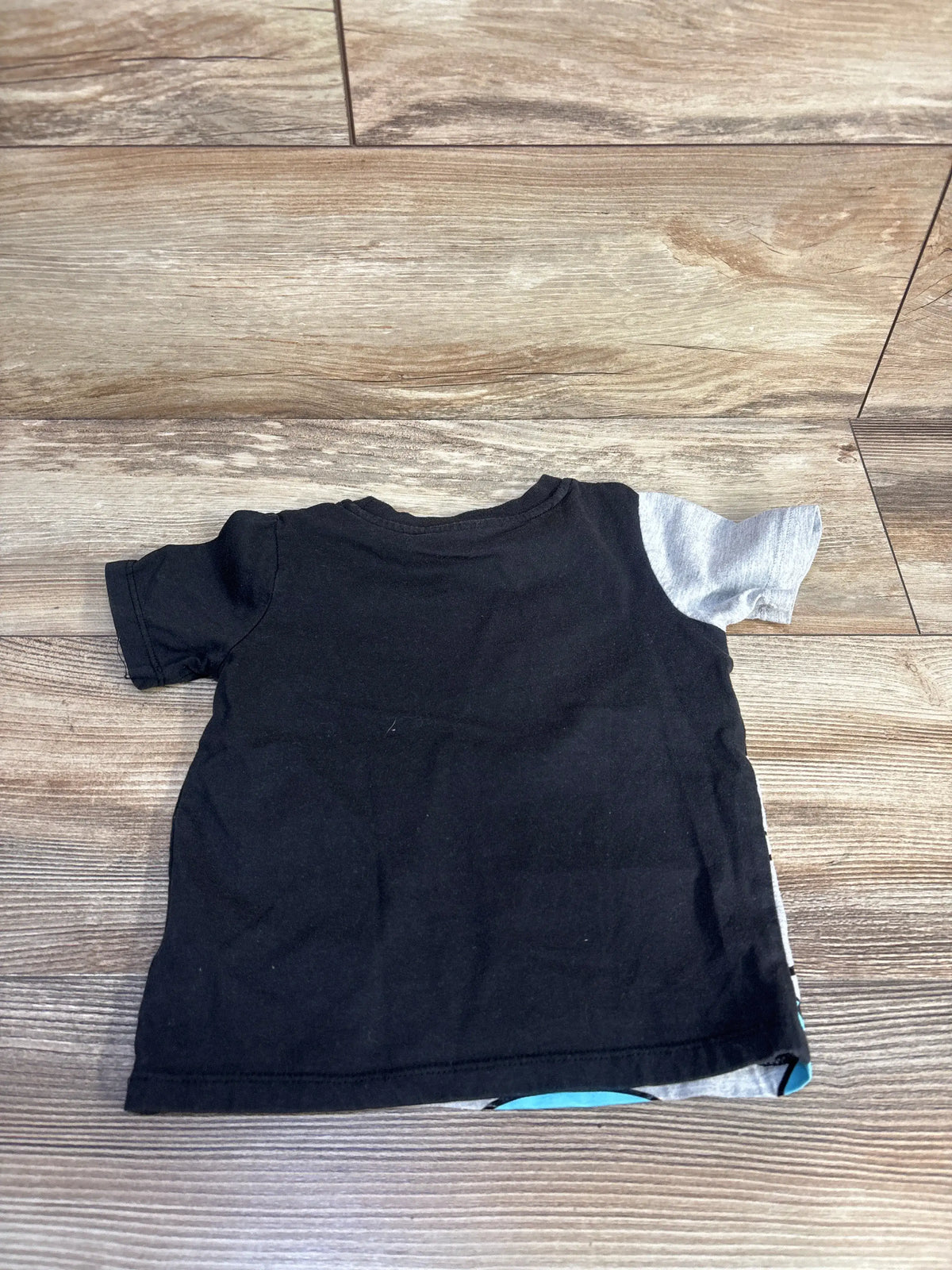 Front view of Disney Mickey and Friends toddler shirt showcasing a black body with gray short sleeves on a wood-look floor