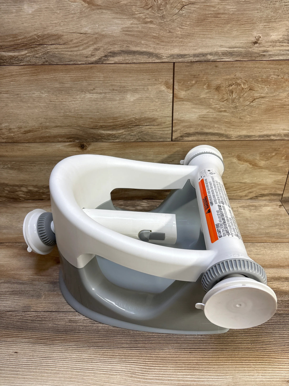 Three-quarter view of Summer Infant My Bath Seat in grey showcasing the front safety bar and suction-cup base with wood floor background