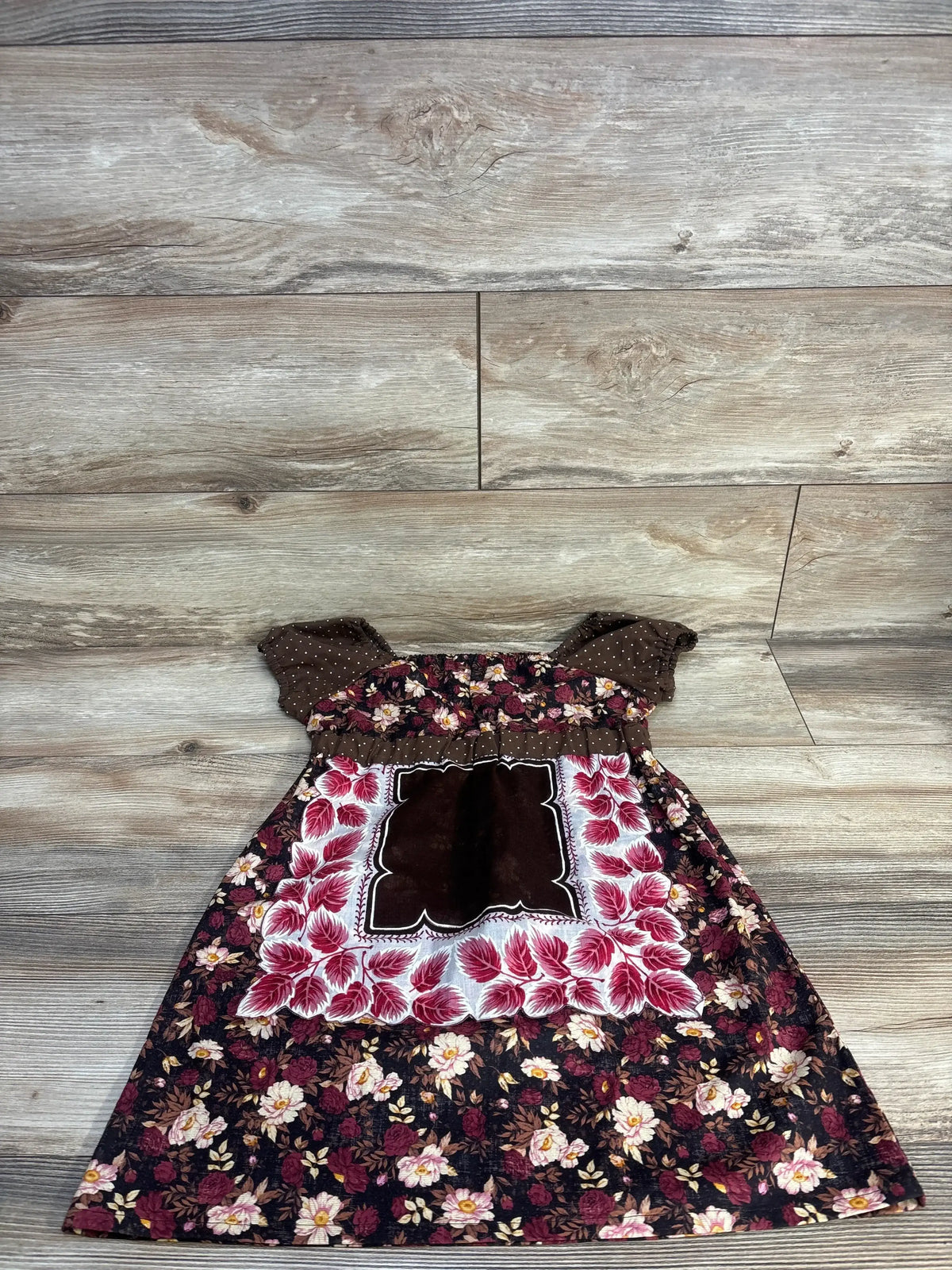 Floral toddler dress with brown polka dot sleeves and leaf applique, laid on wood floor