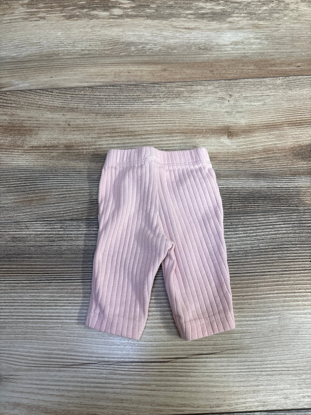Front view of Just One You pink ribbed pants in Preemie size showcasing elastic waistband and ribbed texture on a wood grain background