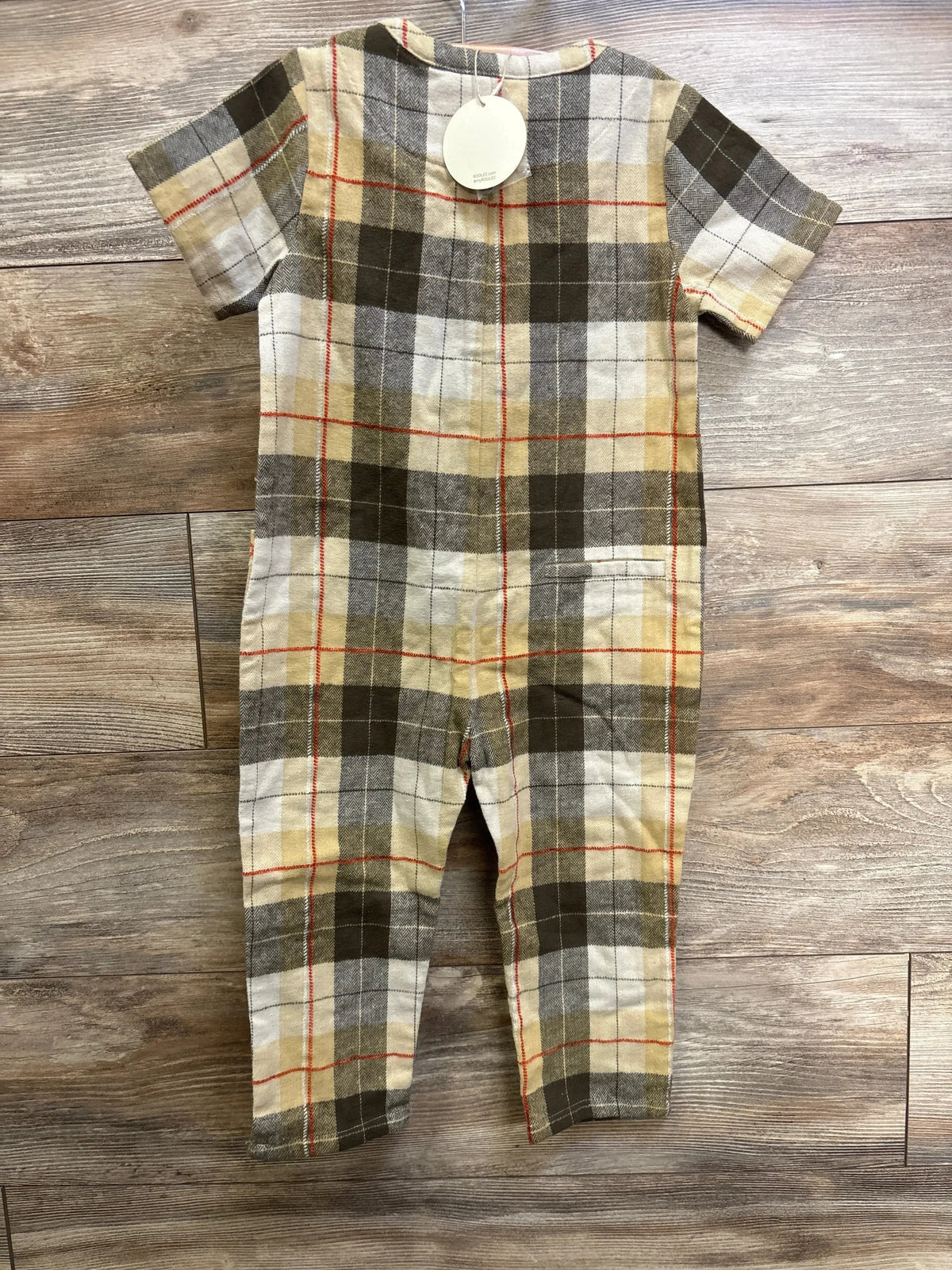 Flat-lay of beige and brown plaid short-sleeve kids jumpsuit (size 5T) showing hip pockets and thin red accent stripes on wood floor background