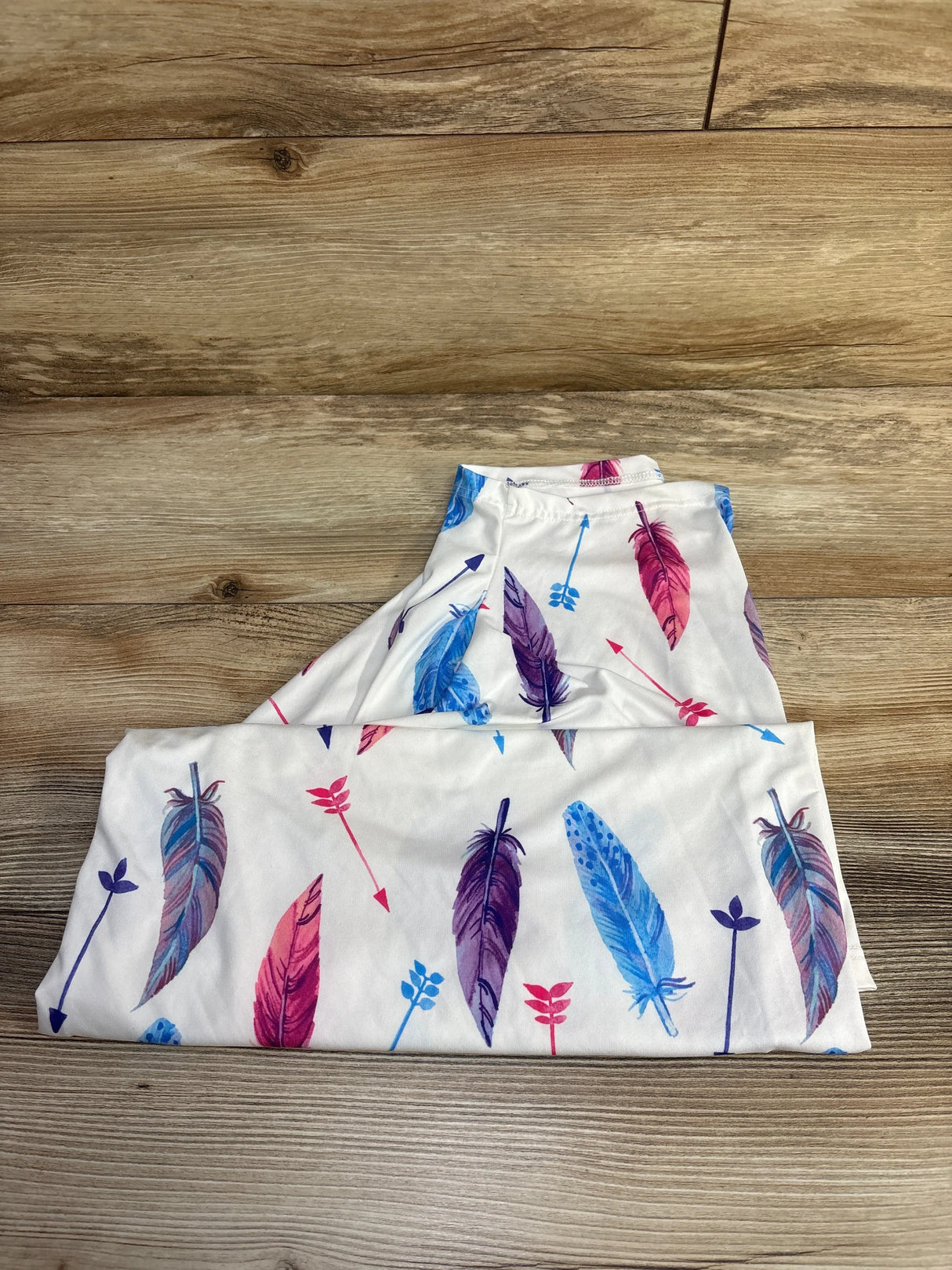 Folded Gufix Multi-Use Cover showcasing colorful pink, purple, and blue feather and arrow print on a wood surface