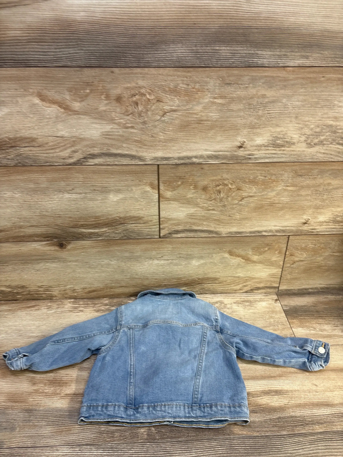 Back view of toddler Old Navy denim jacket showcasing light blue wash, seam detailing, and button cuffs on wood floor