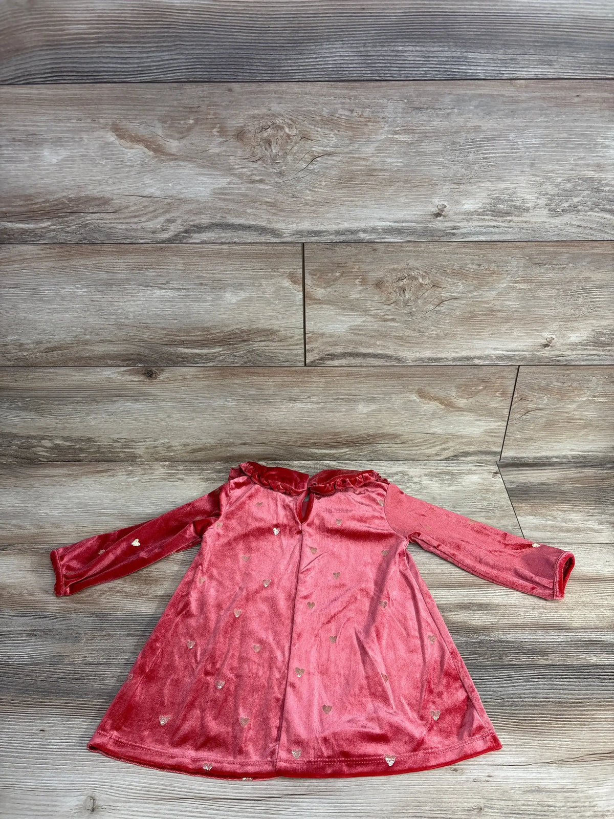 Pink velvet toddler dress with gold heart patterns and long sleeves on wood background