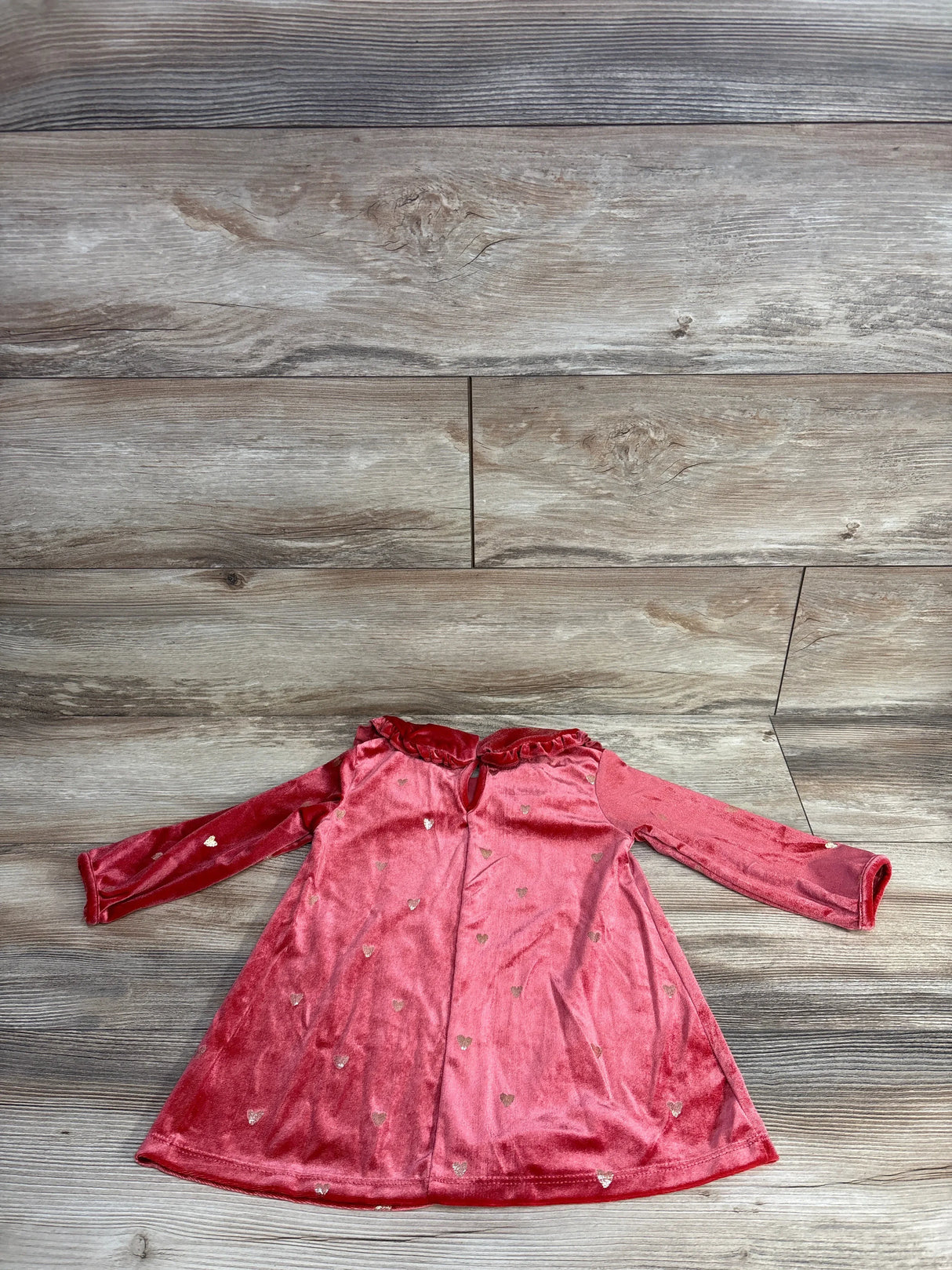 Pink velvet toddler dress with gold heart patterns and long sleeves on wood background