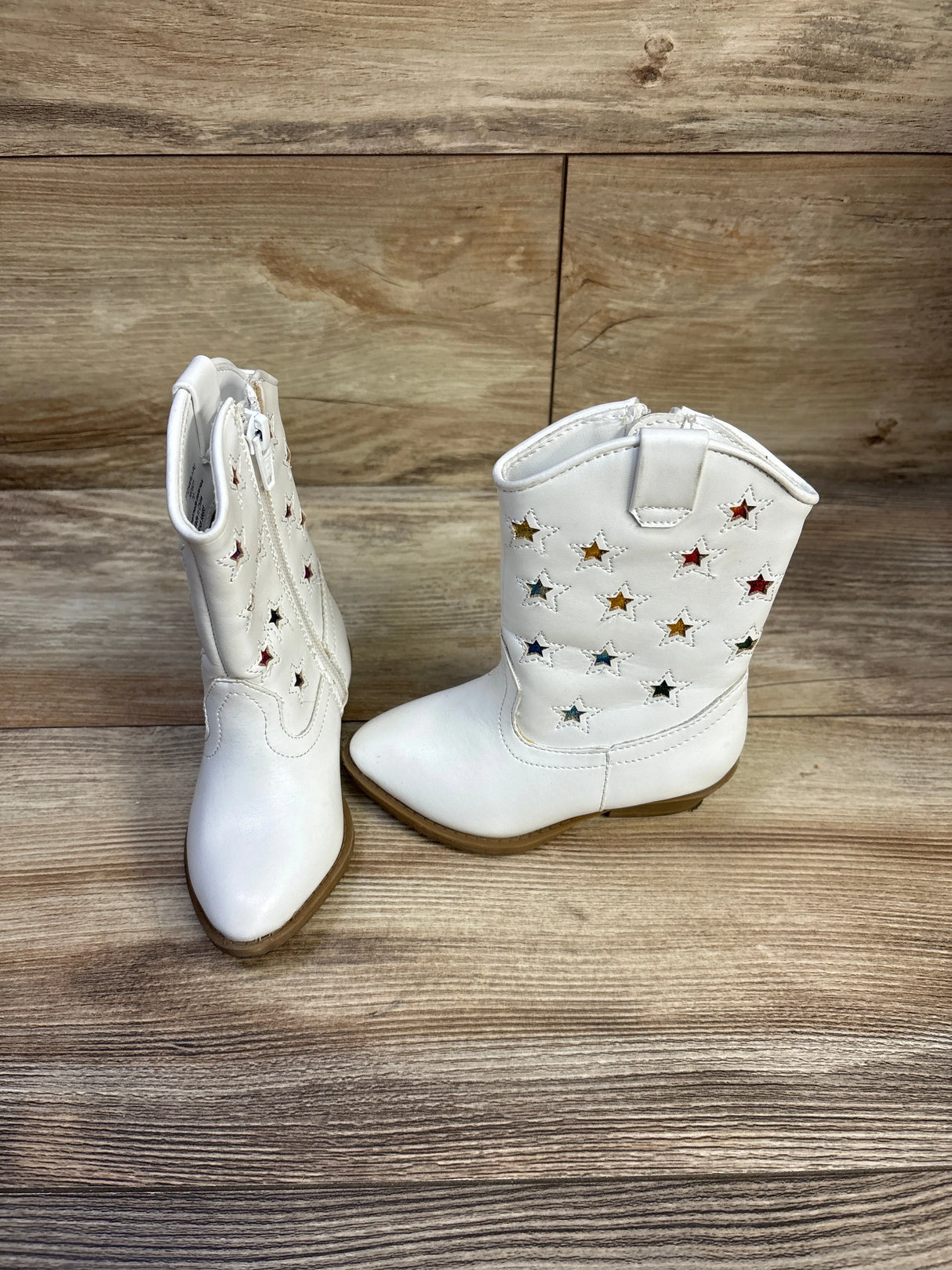 Pair showing front and side of white kids cowgirl boots 7C with star cutouts and multicolor foil backing on wood background