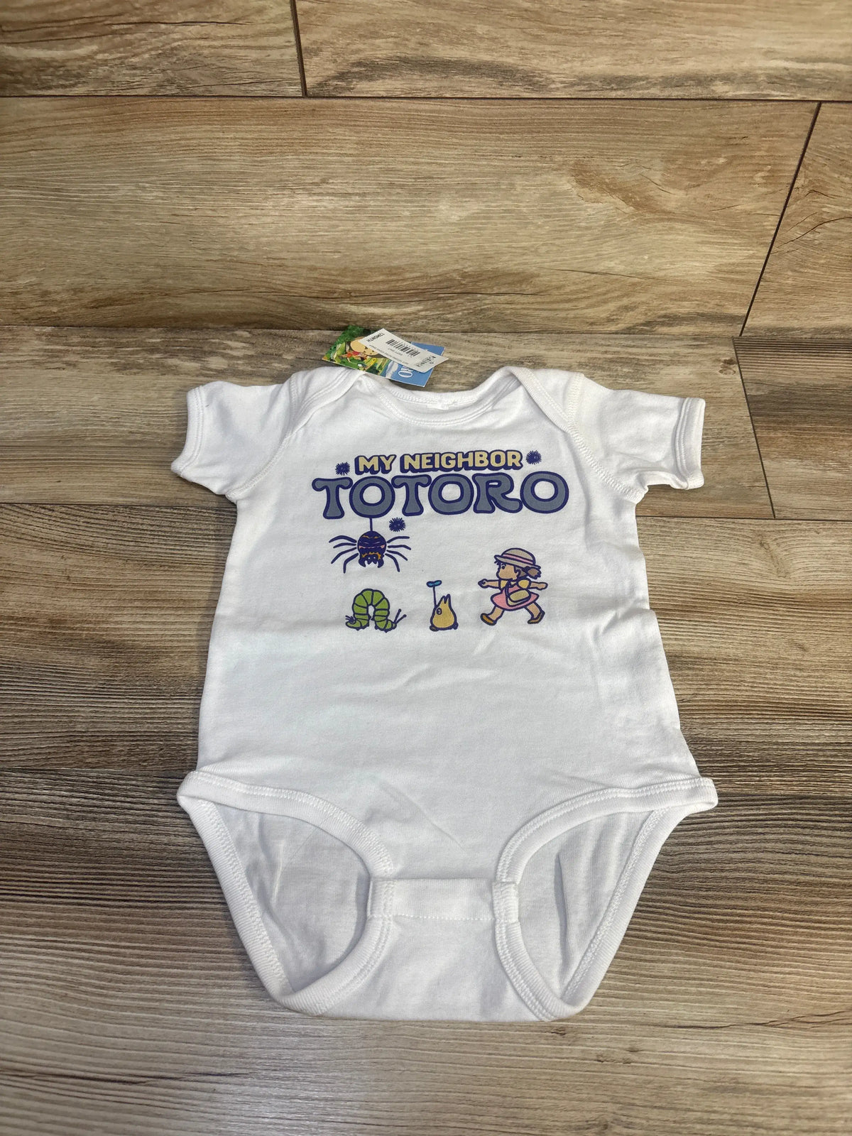 Front view of a white My Neighbor Totoro bodysuit showcasing Studio Ghibli artwork on a wood-look floor