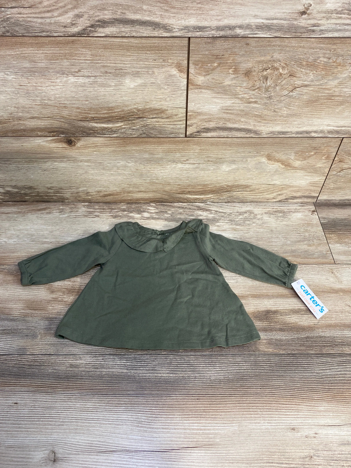 Olive green Carter's long sleeve baby shirt on wood background