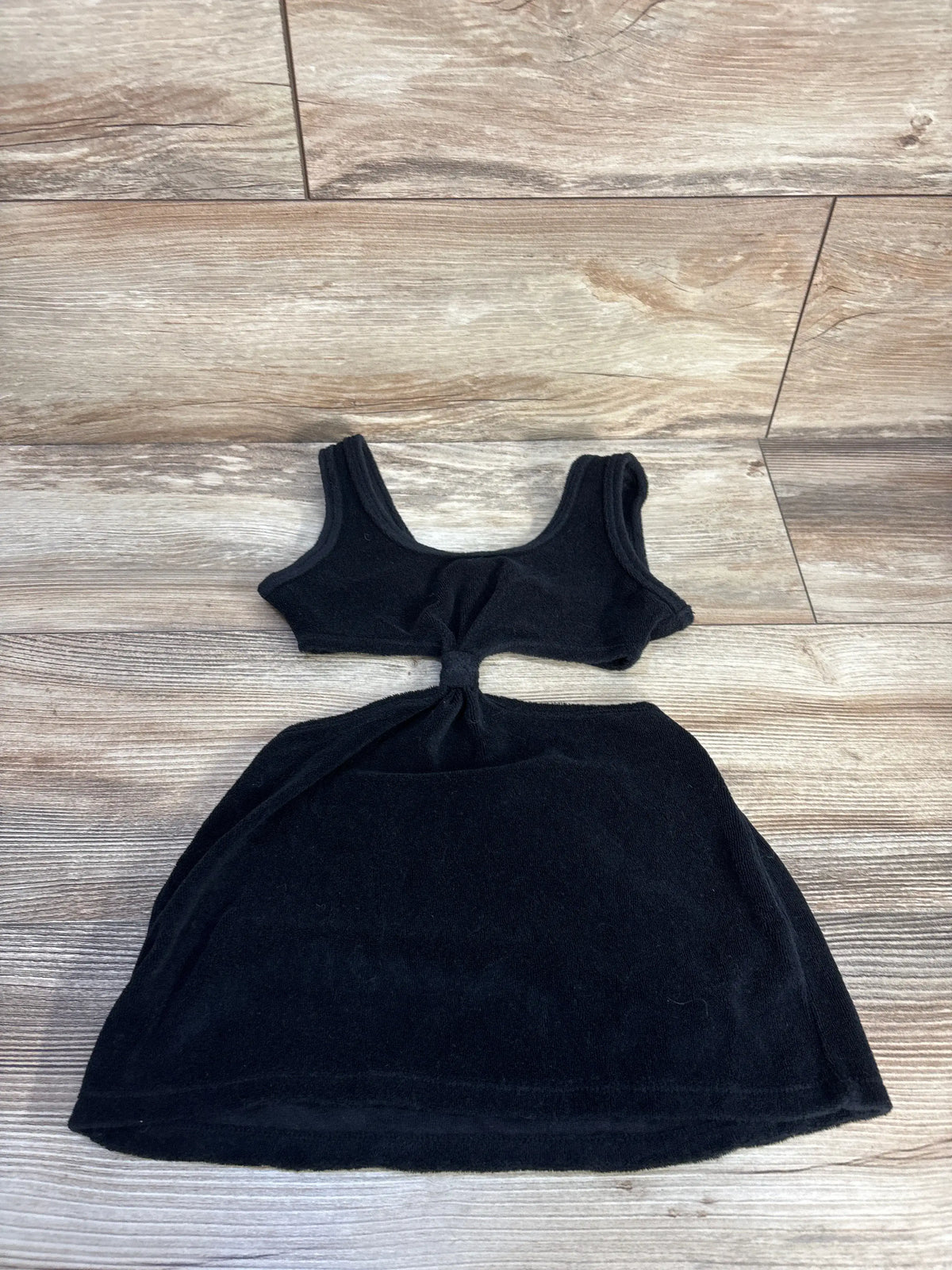 Top-down view of toddler black terry cloth swim cover-up with front knot cutout and tank straps on wood floor