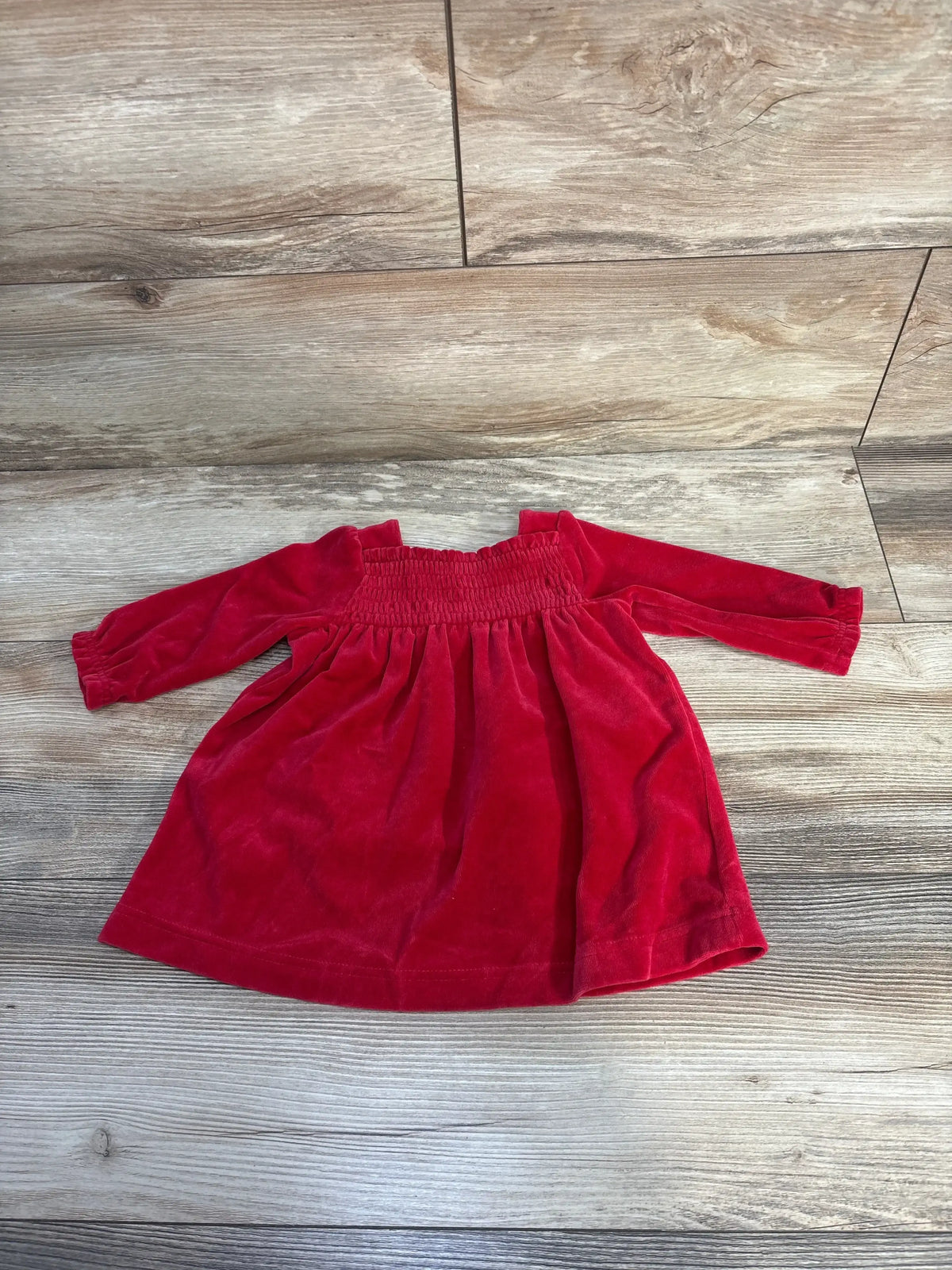 Red long-sleeve velvet toddler dress with smocked bodice on wooden floor