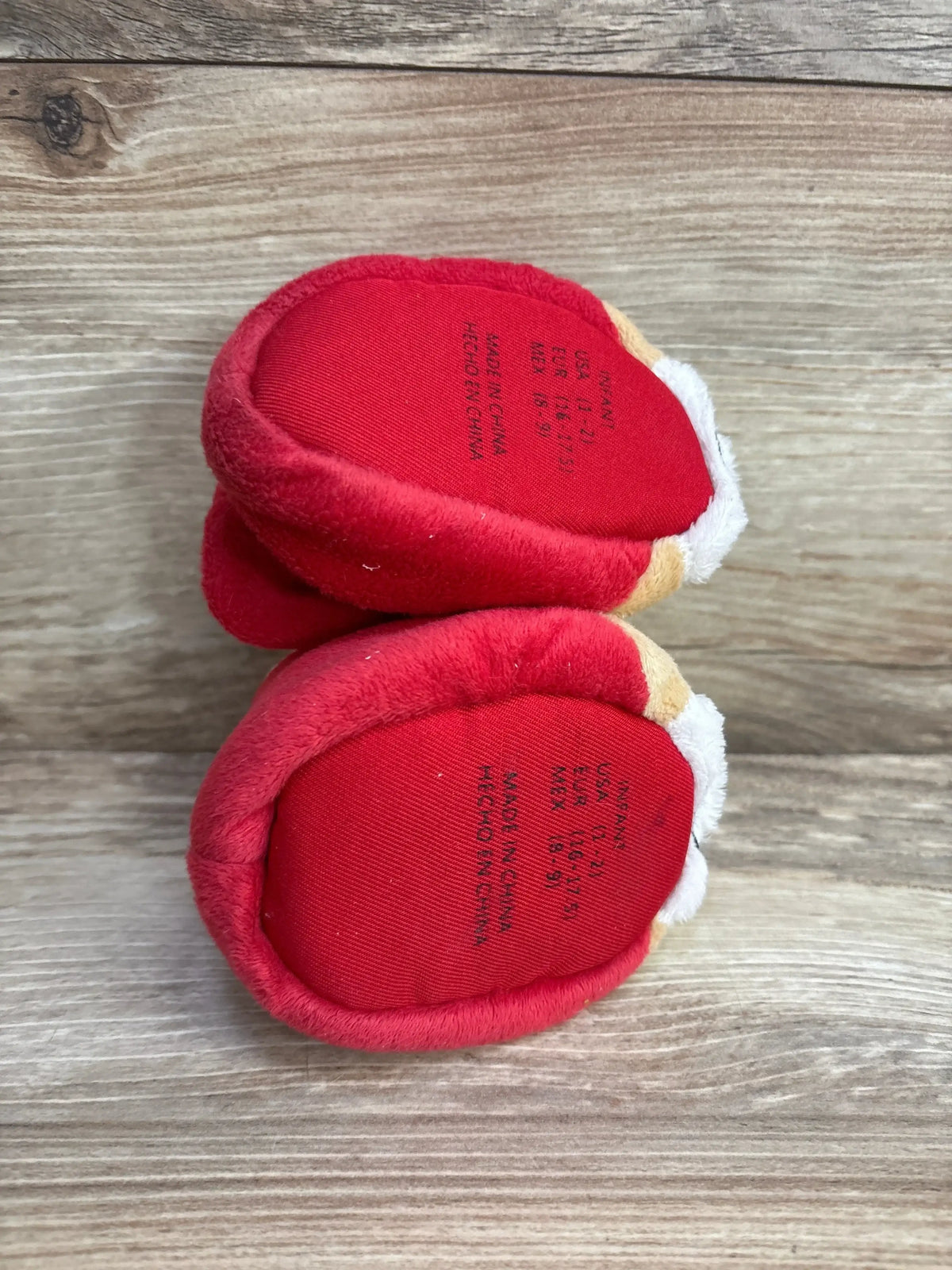 Red infant booties with white trim, size info visible, on wood surface