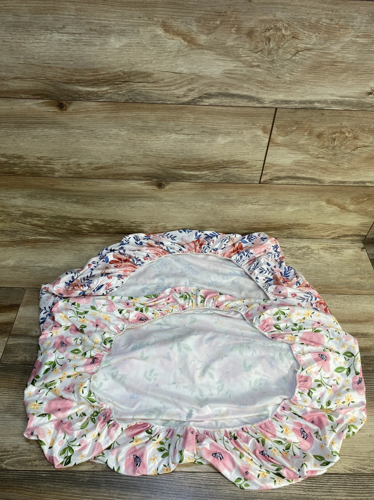 Floral fitted crib sheets with pink and blue patterns on wood floor