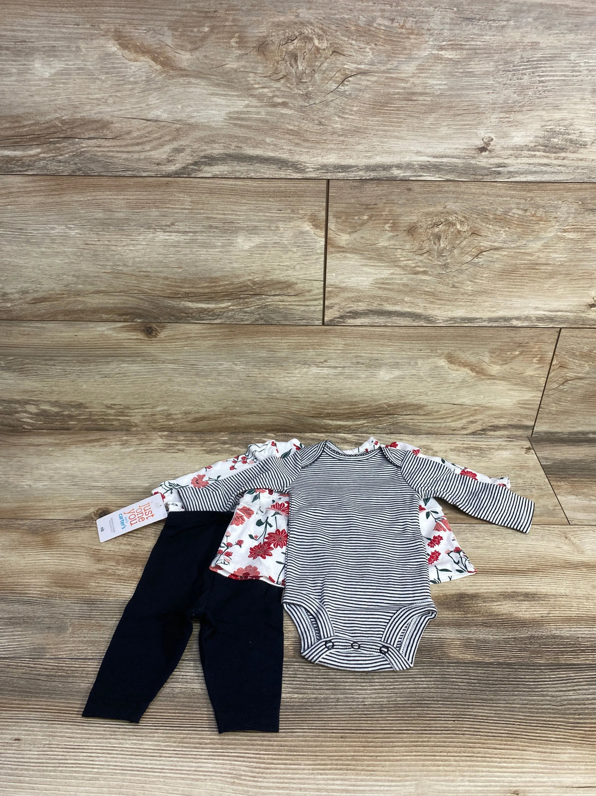 Baby outfit set with striped onesie, floral shirt, and navy leggings on wood background