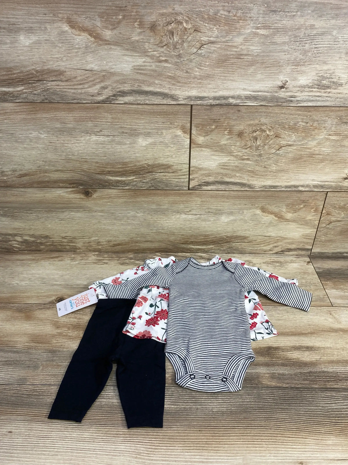 Baby outfit set with striped onesie, floral shirt, and navy leggings on wood background