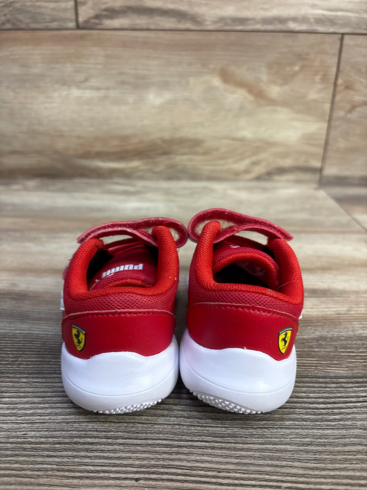 Rear view of red Puma x Scuderia Ferrari Kart Cat III sneakers showcasing Ferrari logos and white cushioned soles on wood flooring