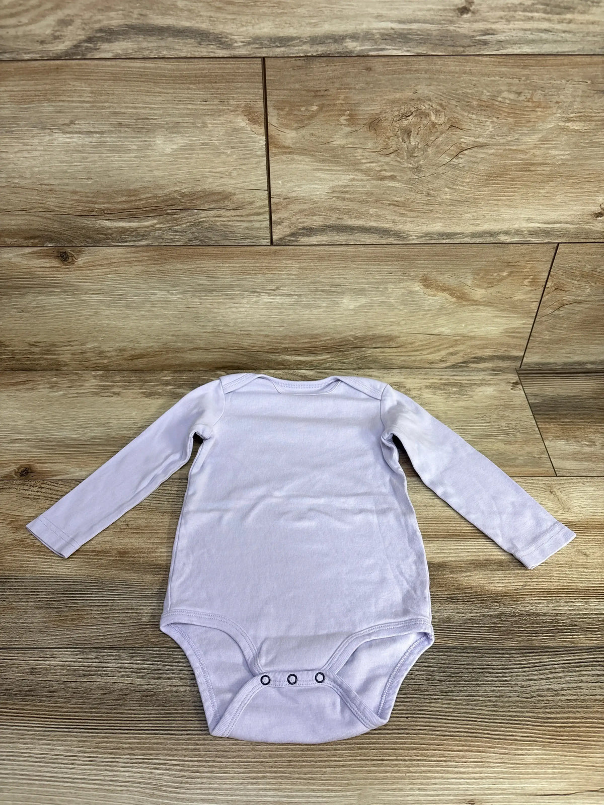 Light purple long sleeve baby bodysuit with snaps on wood floor background