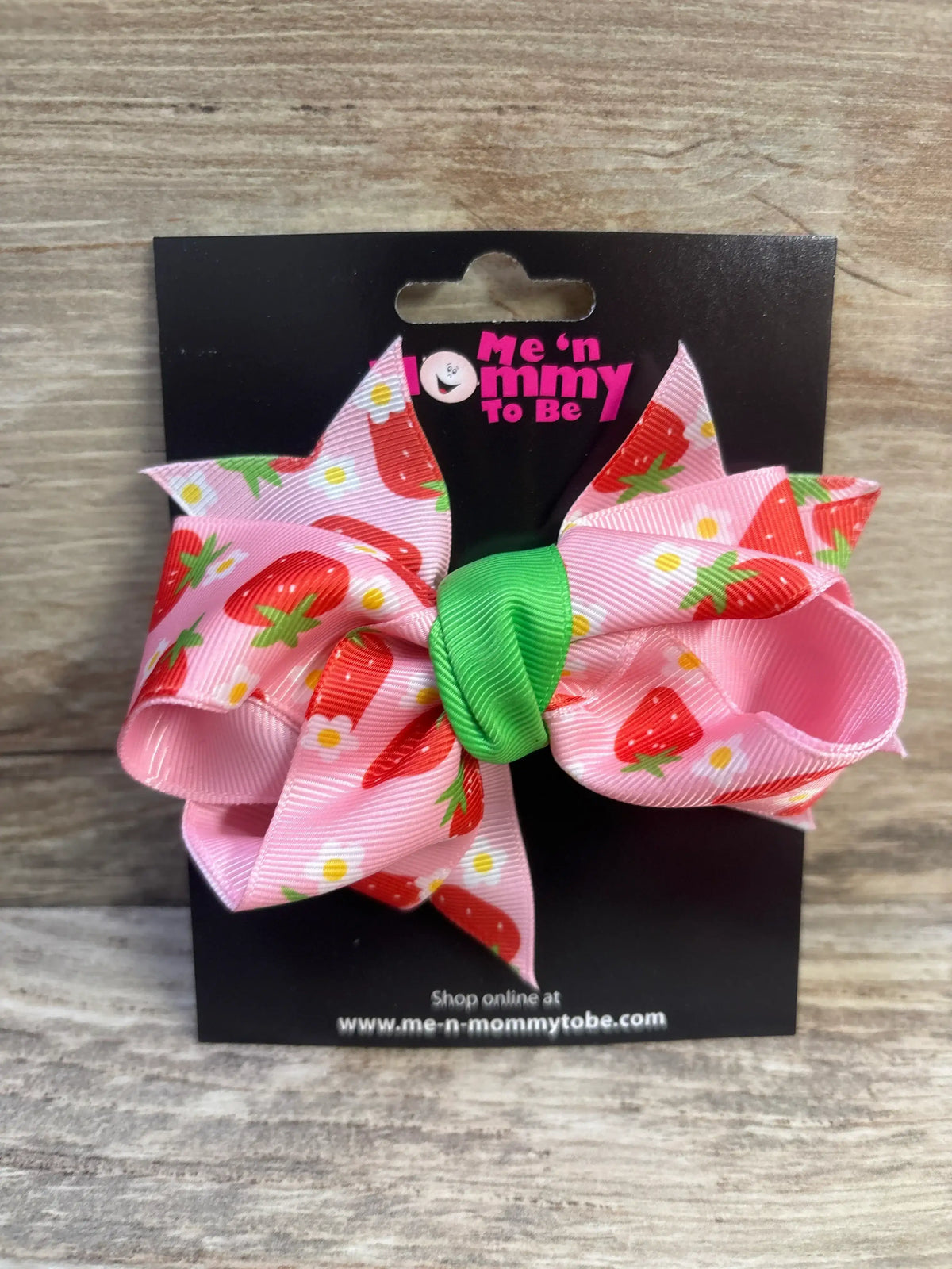 Front view of large strawberry hair bow showing pink grosgrain ribbon with strawberry print and green center knot on black display card