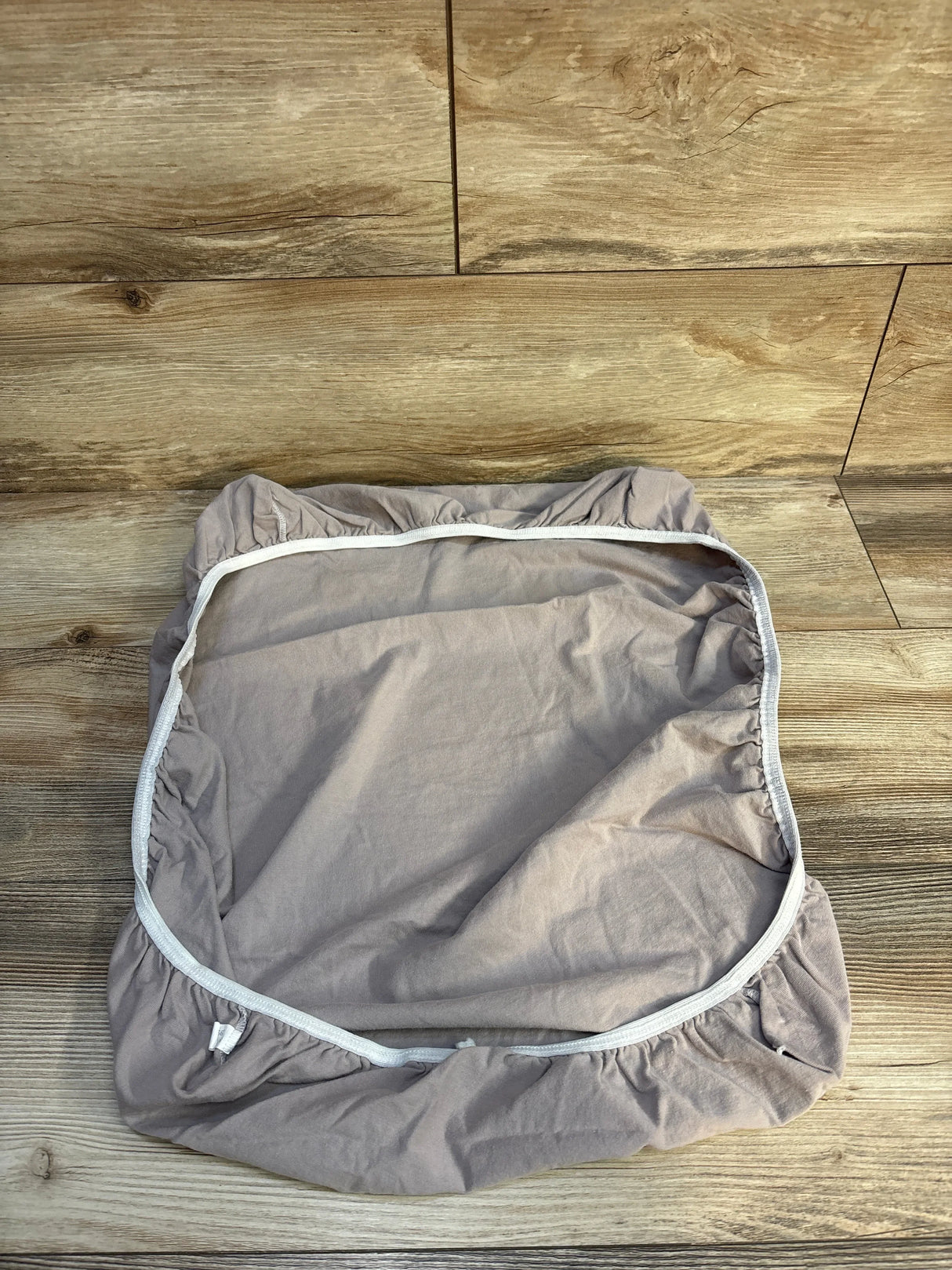Beige fitted sheet with elastic edges laid flat on wooden floor with natural grain