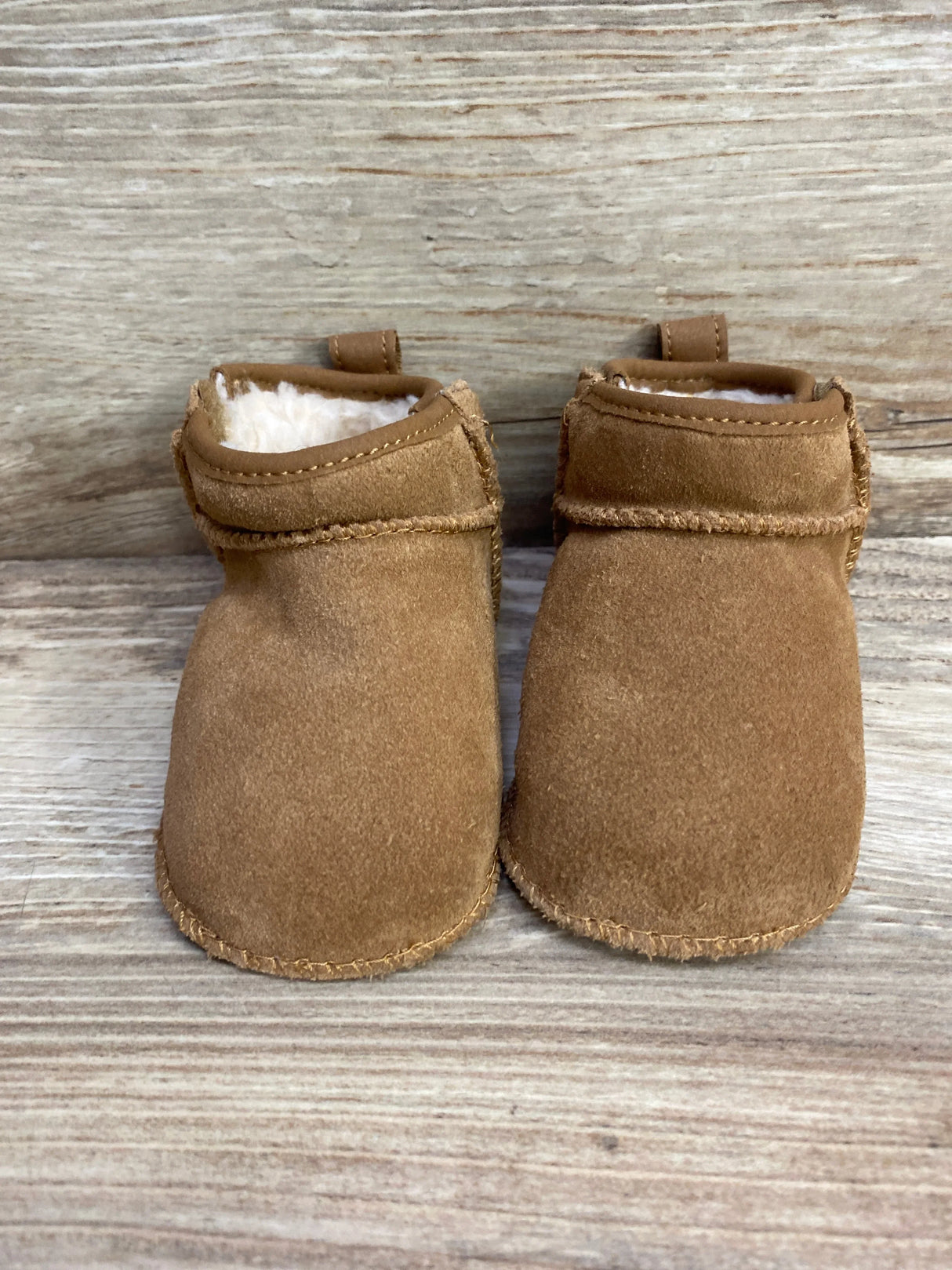Pair of brown suede baby moccasin booties with soft white lining on wooden surface