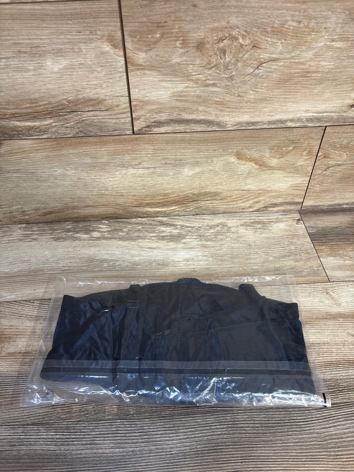 Top view of a black MOMder WEAR nursing bra showcasing its folded shape in clear packaging on a wood-look floor