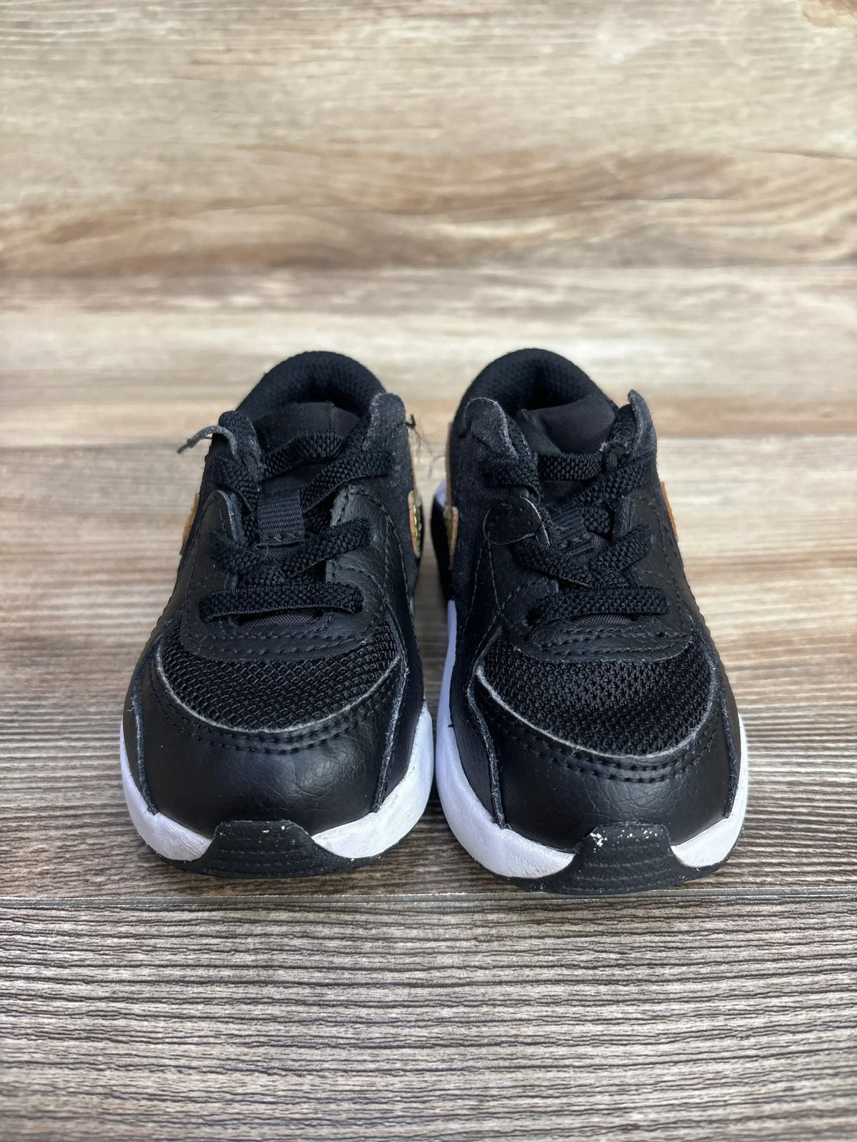 Side view of Nike Air Max Excee TD toddler sneakers with metallic gold star swoosh and white sole on wooden floor