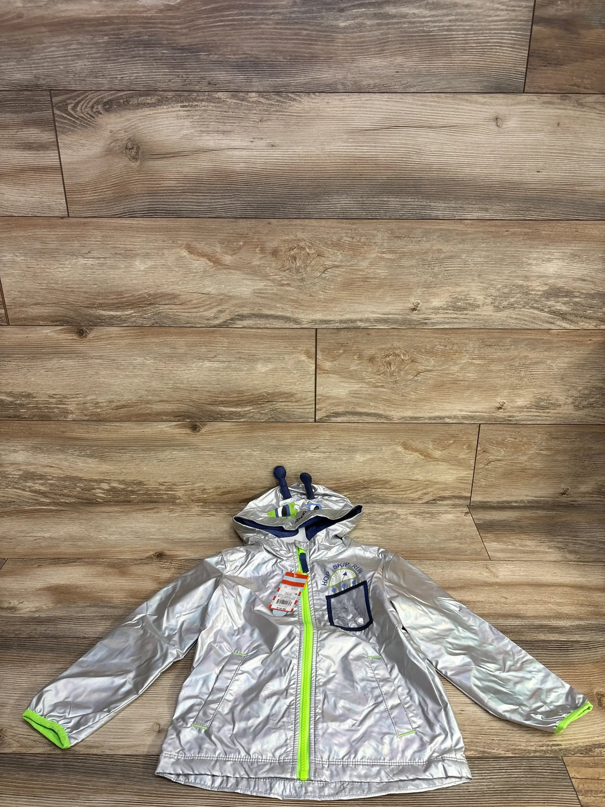 Silver reflective kids raincoat with hood, neon yellow zipper and navy blue pocket on wooden floor