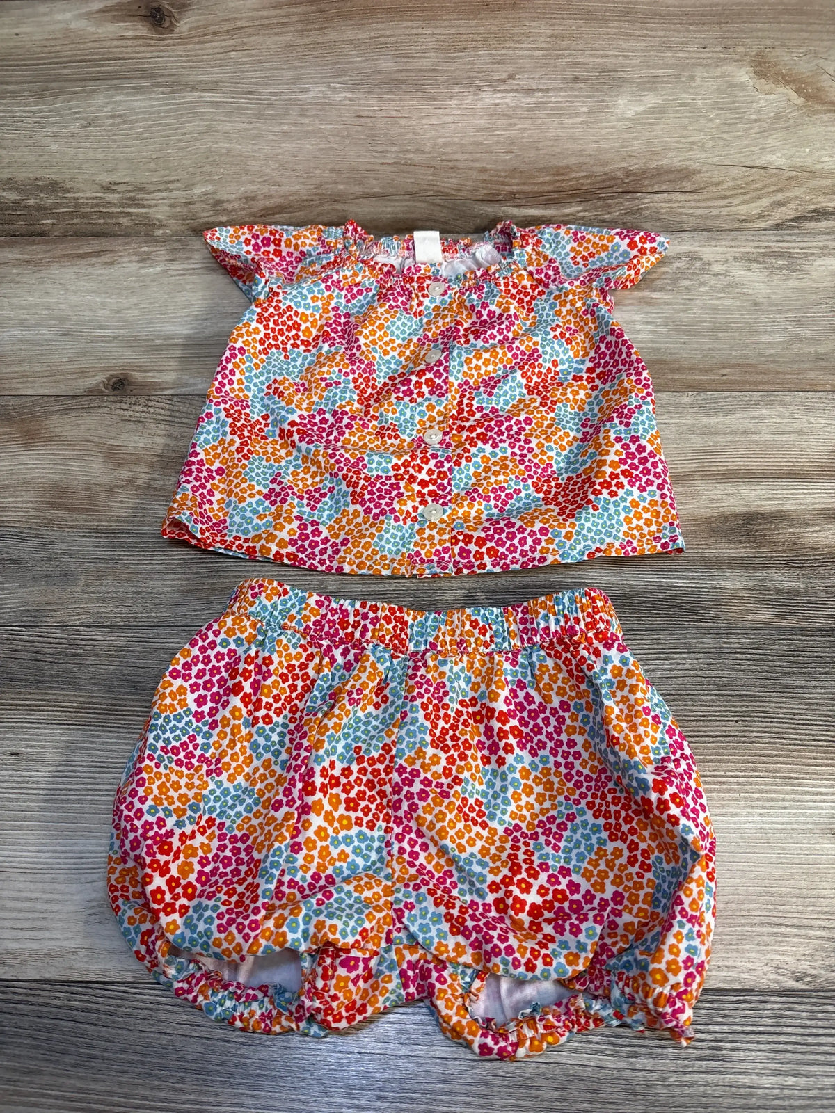 Flat lay of Tucker and Tate girls’ colorful floral button blouse and bloomers showing front buttons, ruffle sleeves, and elastic waist on wood background