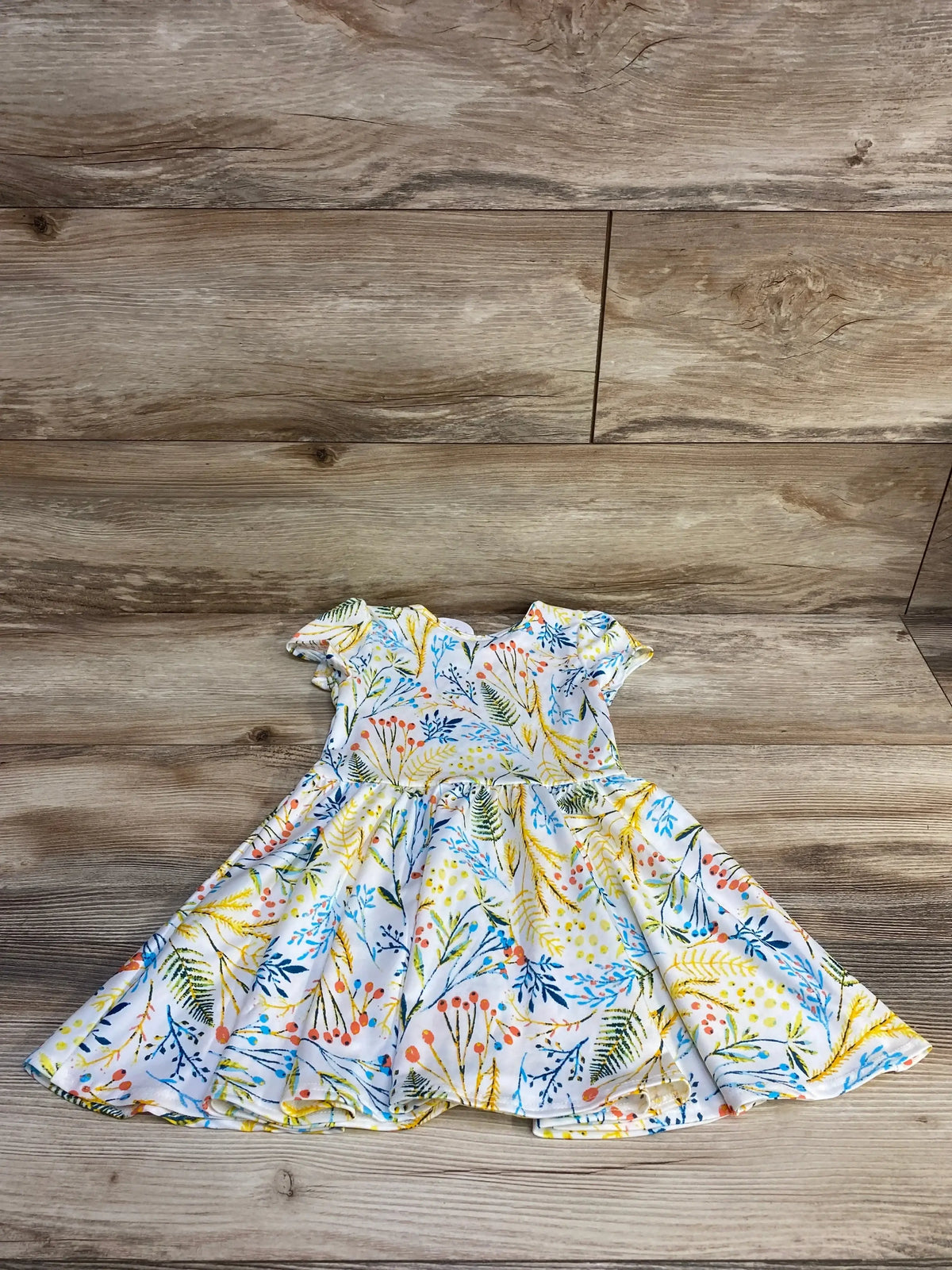 Flat lay of Dot Dot Smile toddler twirl dress showing puff sleeves and full skirt with colorful floral print on wood background