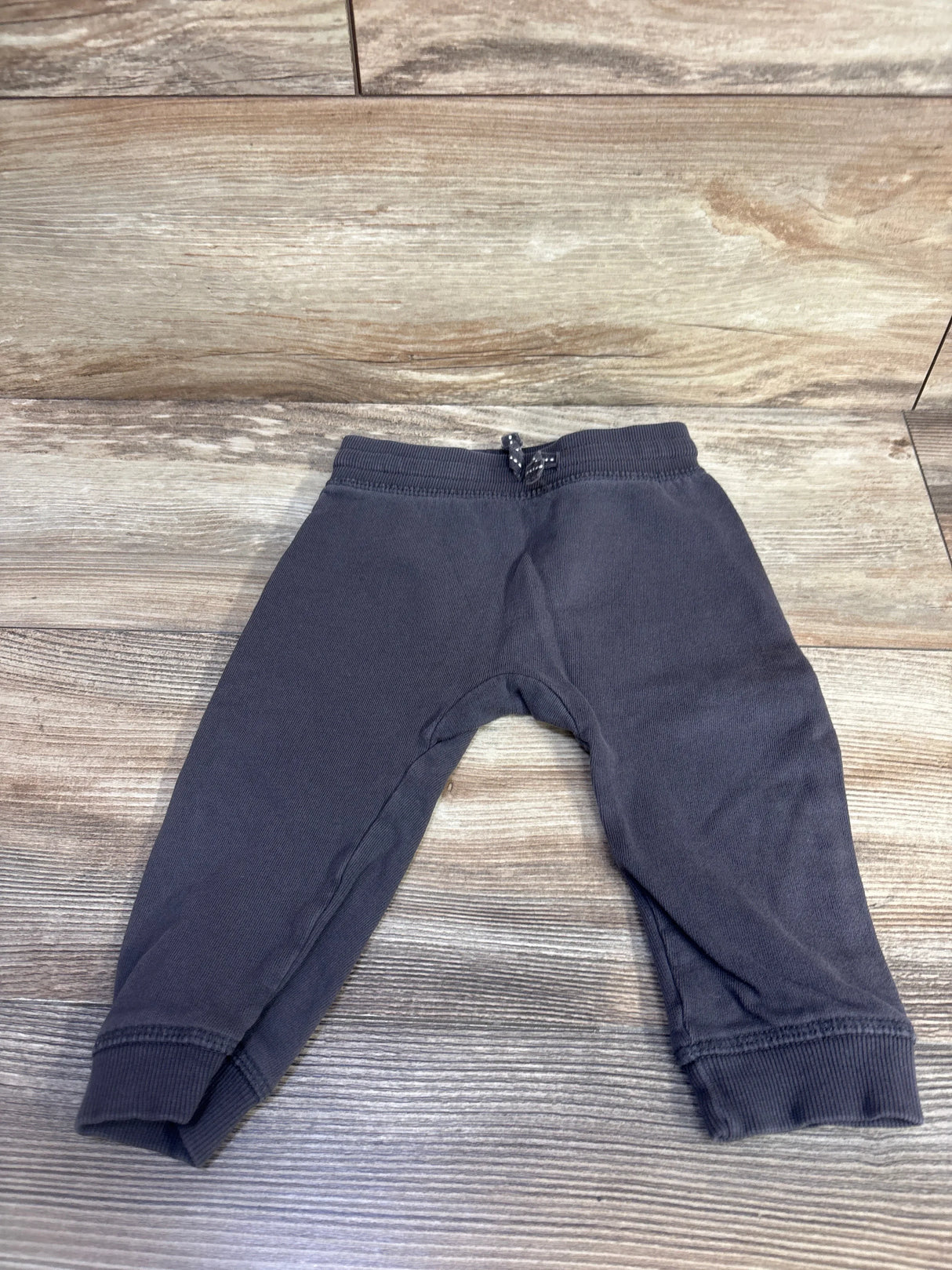 Front view of H&M grey baby drawstring joggers, size 9–12 months, showing elastic waistband with dotted drawstring and ribbed cuffs on wood background