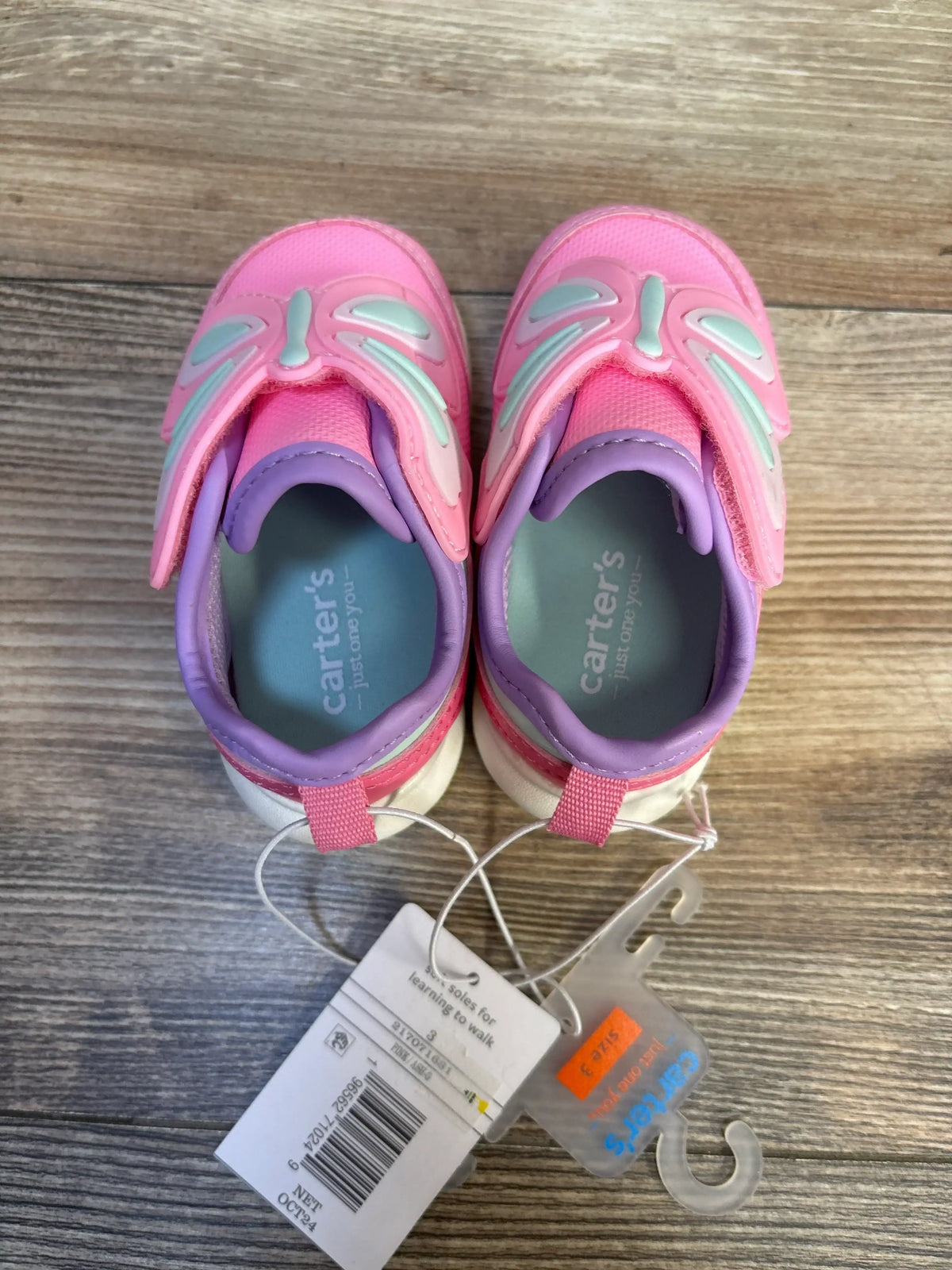Pink and purple Carter's toddler shoes with butterfly design, tags attached, on wood floor