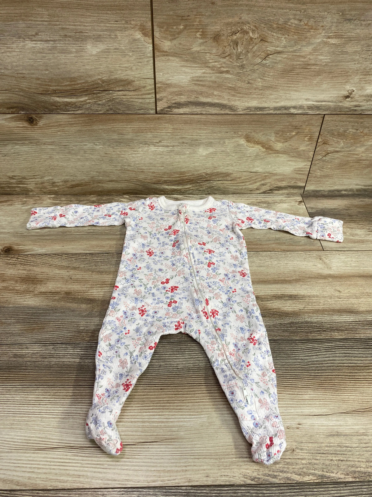 Front view of Cotton On Baby organic floral sleeper, white size 3 to 6 months, with floral print and footed legs on wood floor