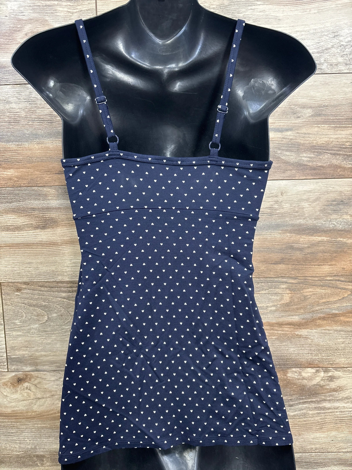 Front view of navy maternity cami with white heart print and adjustable straps on a black mannequin torso against a wood floor