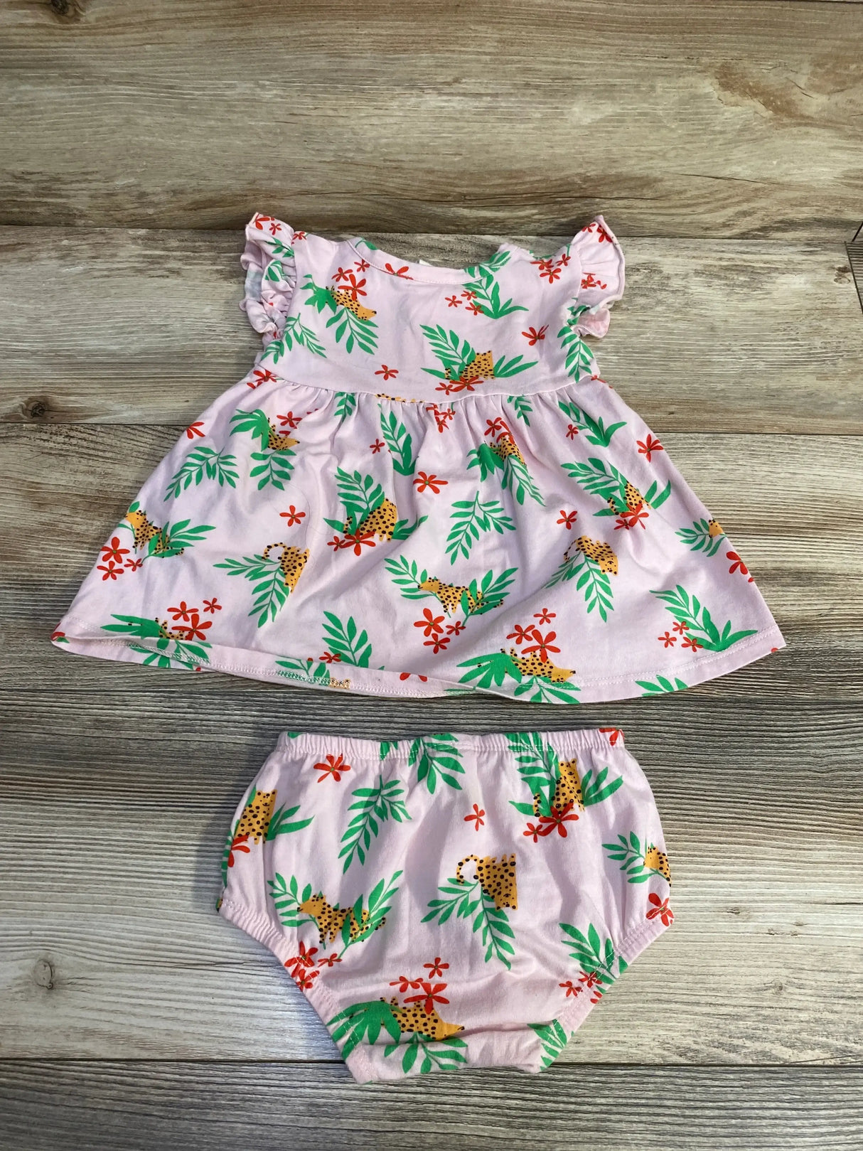 Flat lay of pink Tucker + Tate henley dress and matching bloomers showing ruffle cap sleeves, gathered skirt, and tropical leaf and cheetah print on wood background