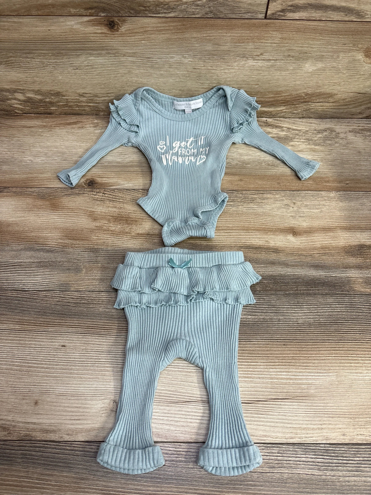 Light blue ribbed baby outfit with ruffle sleeves and text saying "I got it from my mama" laid on wooden surface