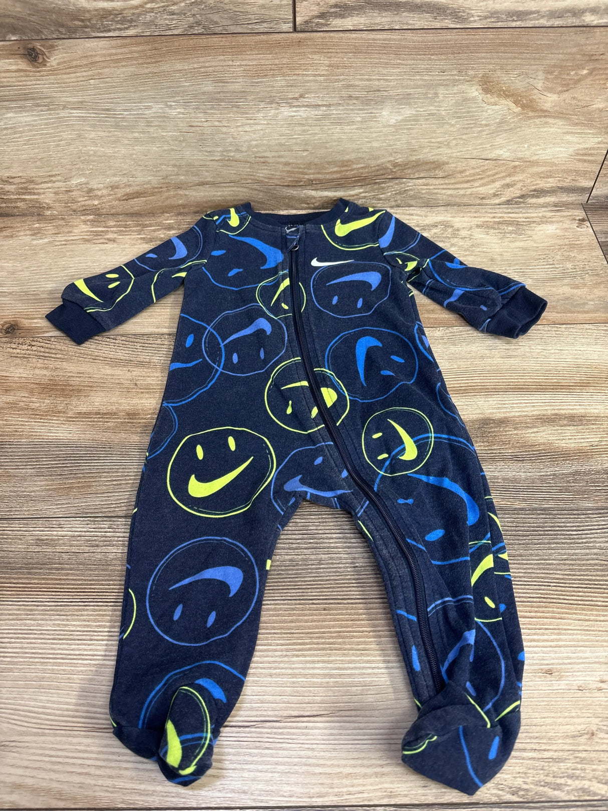 Navy blue baby footed sleeper with blue and yellow smiley face print on wood background