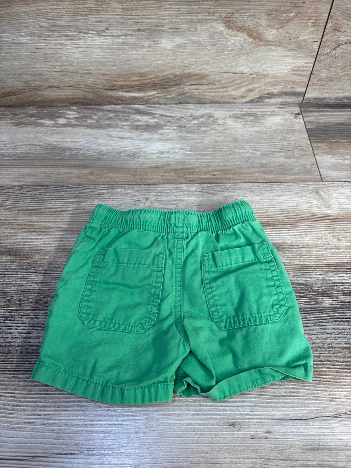 Back view of Cat & Jack green toddler drawstring shorts showing elastic waistband and two back patch pockets on light wood floor