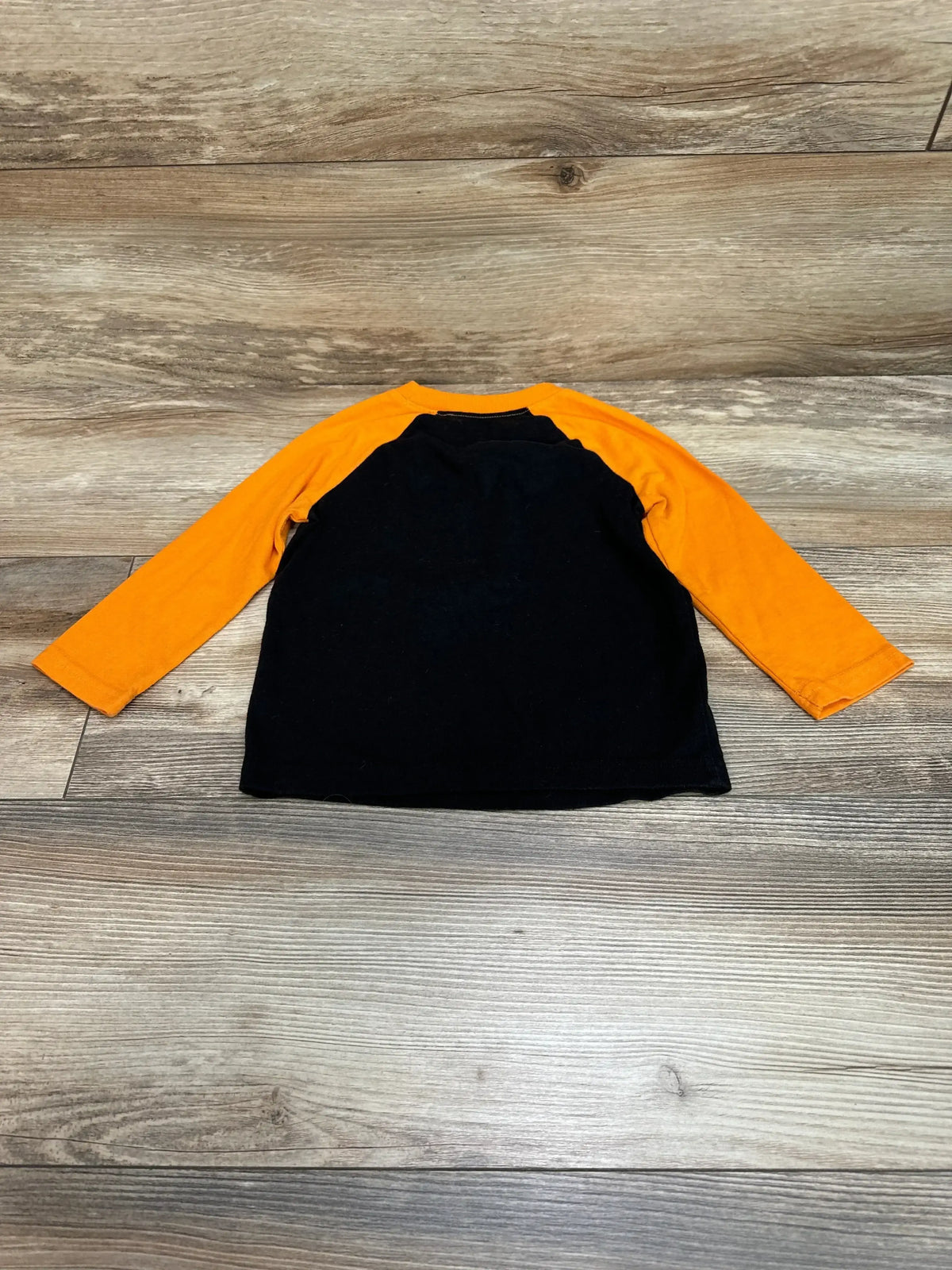 Front view of Jumping Beans Boo Crew shirt showcasing a black body and orange long sleeves on a wood-patterned background