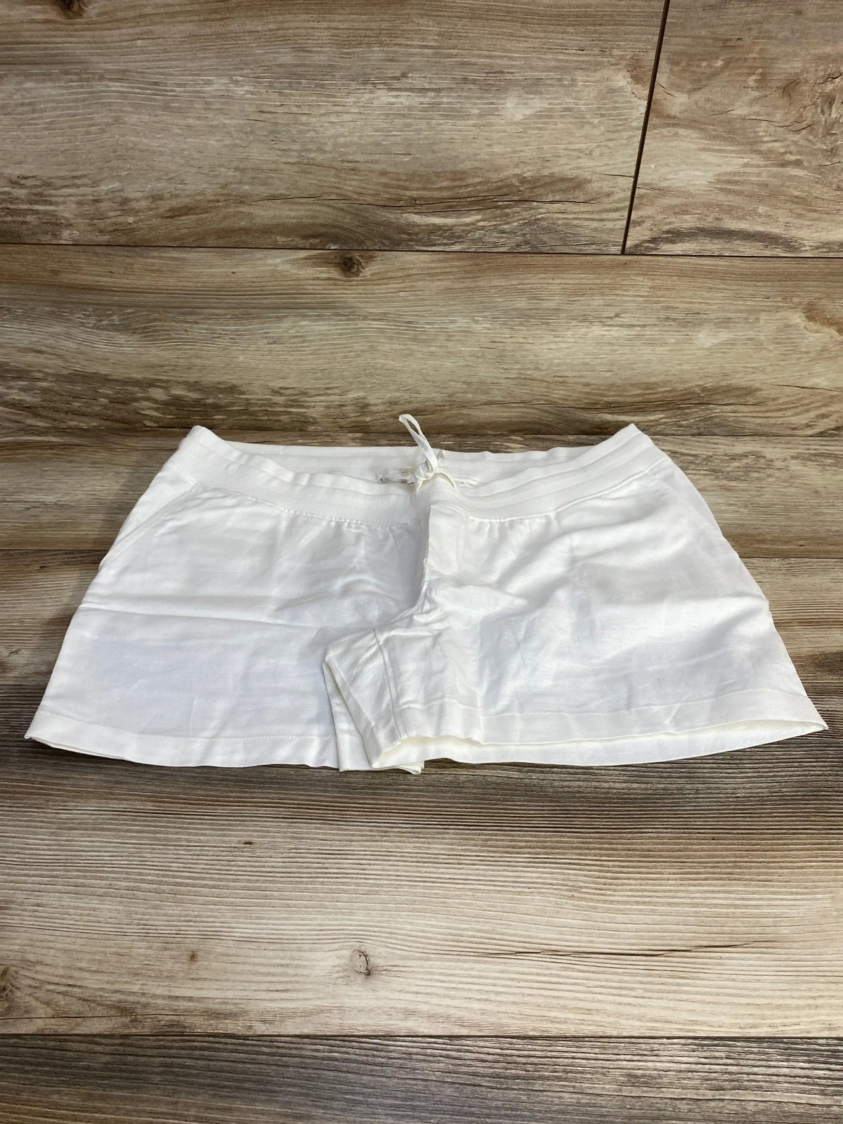 Flat lay of Gap maternity linen-cotton shorts showing elastic drawstring waist and white fabric on wood background
