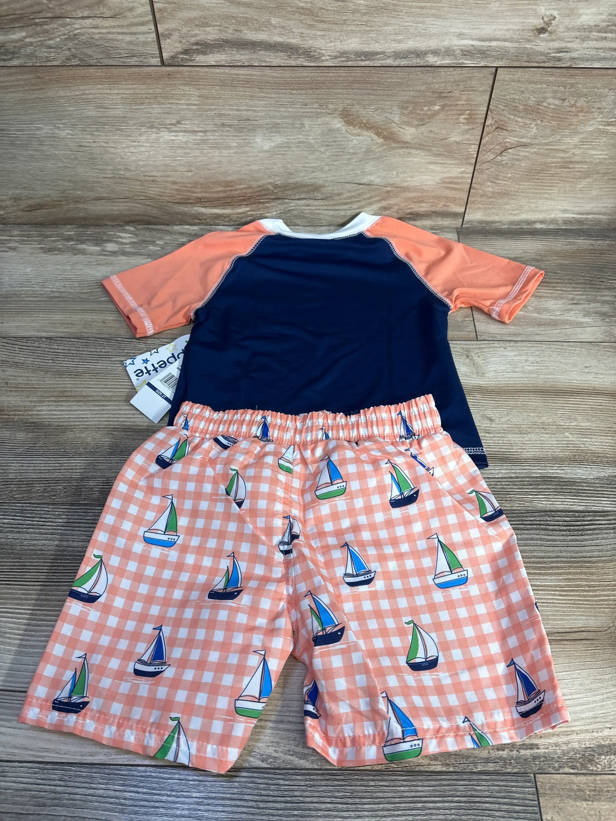Front view of Wippette two-piece swim set showcasing short sleeve rash guard and matching navy swim trunks on wood floor