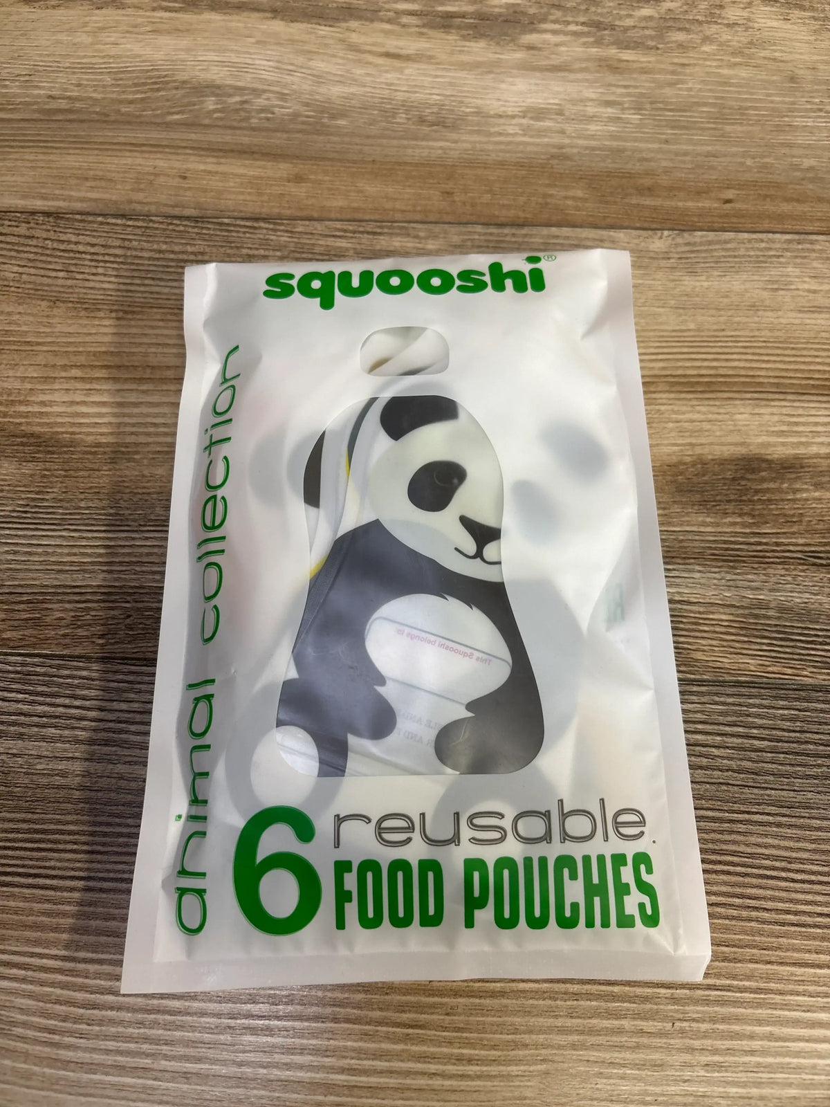 Front view of Squooshi 6oz reusable food pouches 6 pack showing panda pouch visible through frosted package on wood floor