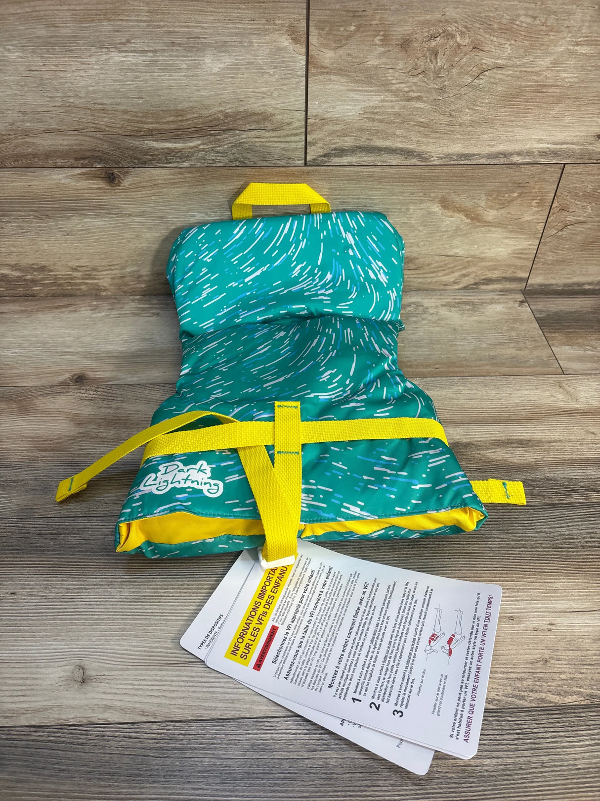 Kids' teal and yellow life jacket with safety tag on wood floor.