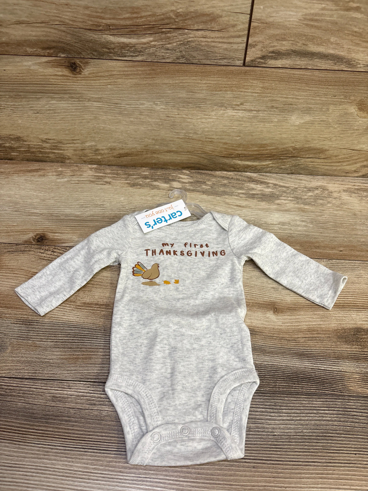 Front view of gray newborn Thanksgiving bodysuit with My First Thanksgiving text, turkey graphic, and snap closures on wood