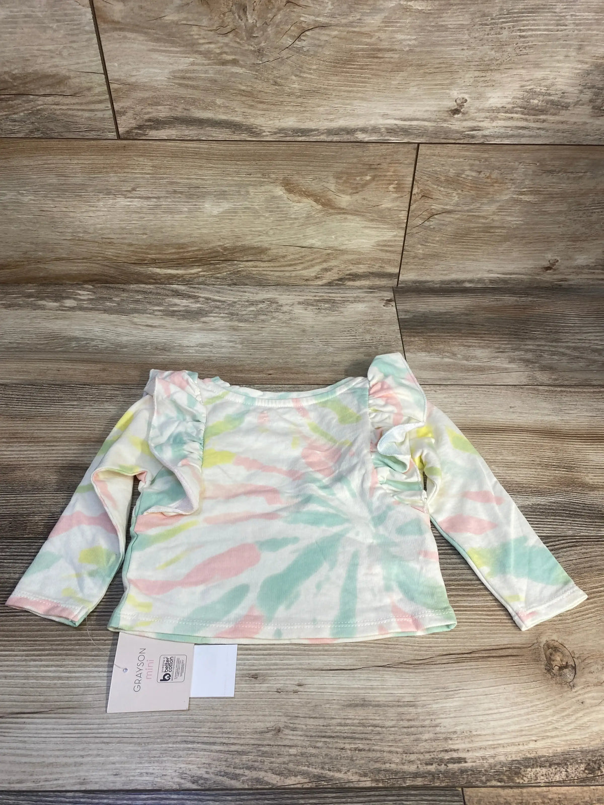 Pastel tie-dye long sleeve baby shirt with ruffled shoulders on wood background