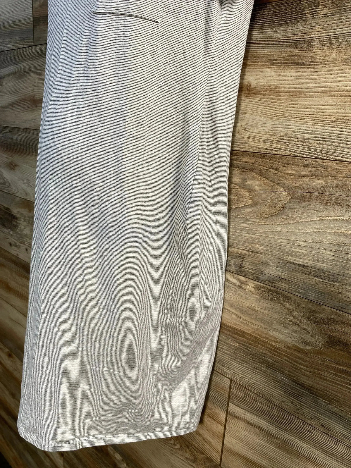 Close-up side view of grey and white striped maternity dress showing thin horizontal stripes, side seam and pocket detail against wood plank background