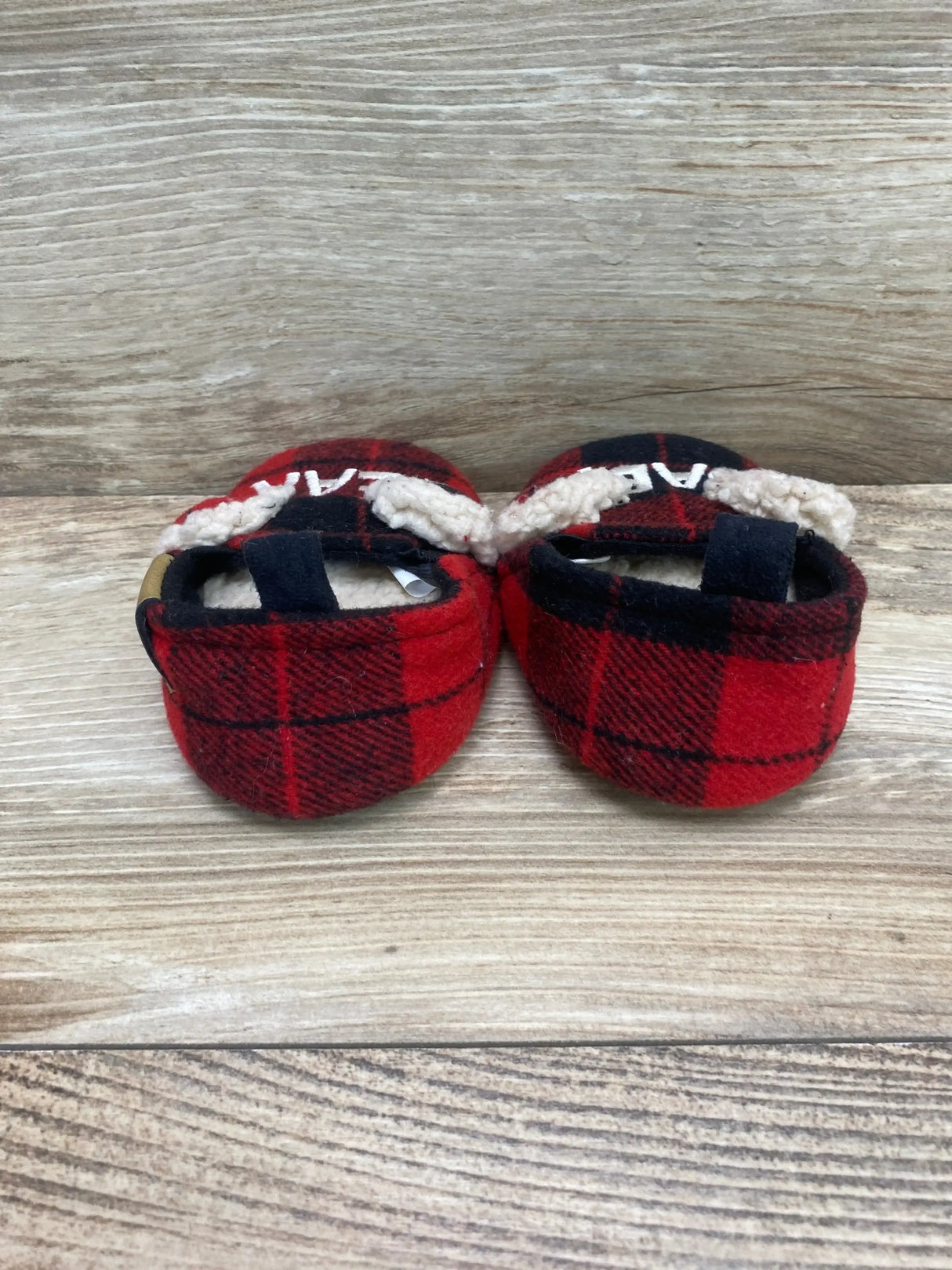 Back view of Dearfoams baby bear slippers size 4C showing red and black plaid with cream sherpa trim on light wood