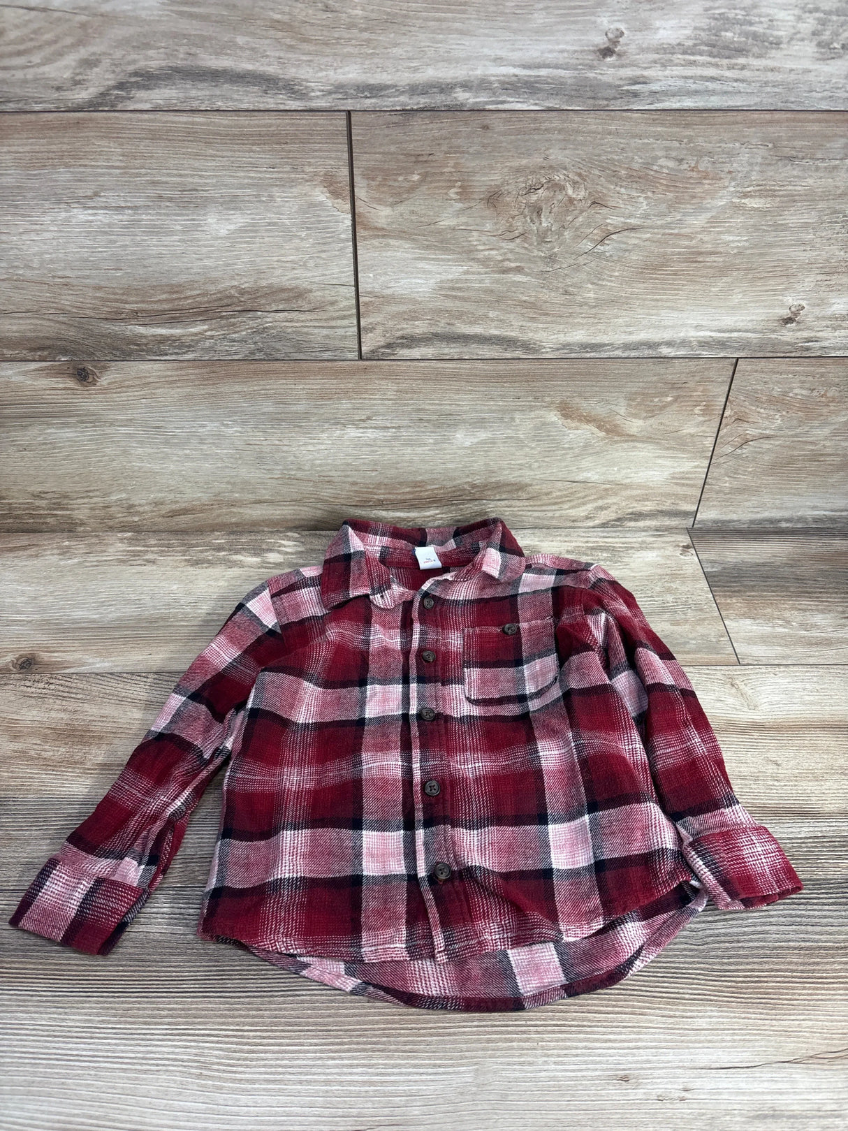Red and black plaid long sleeve button-up toddler shirt on wooden background
