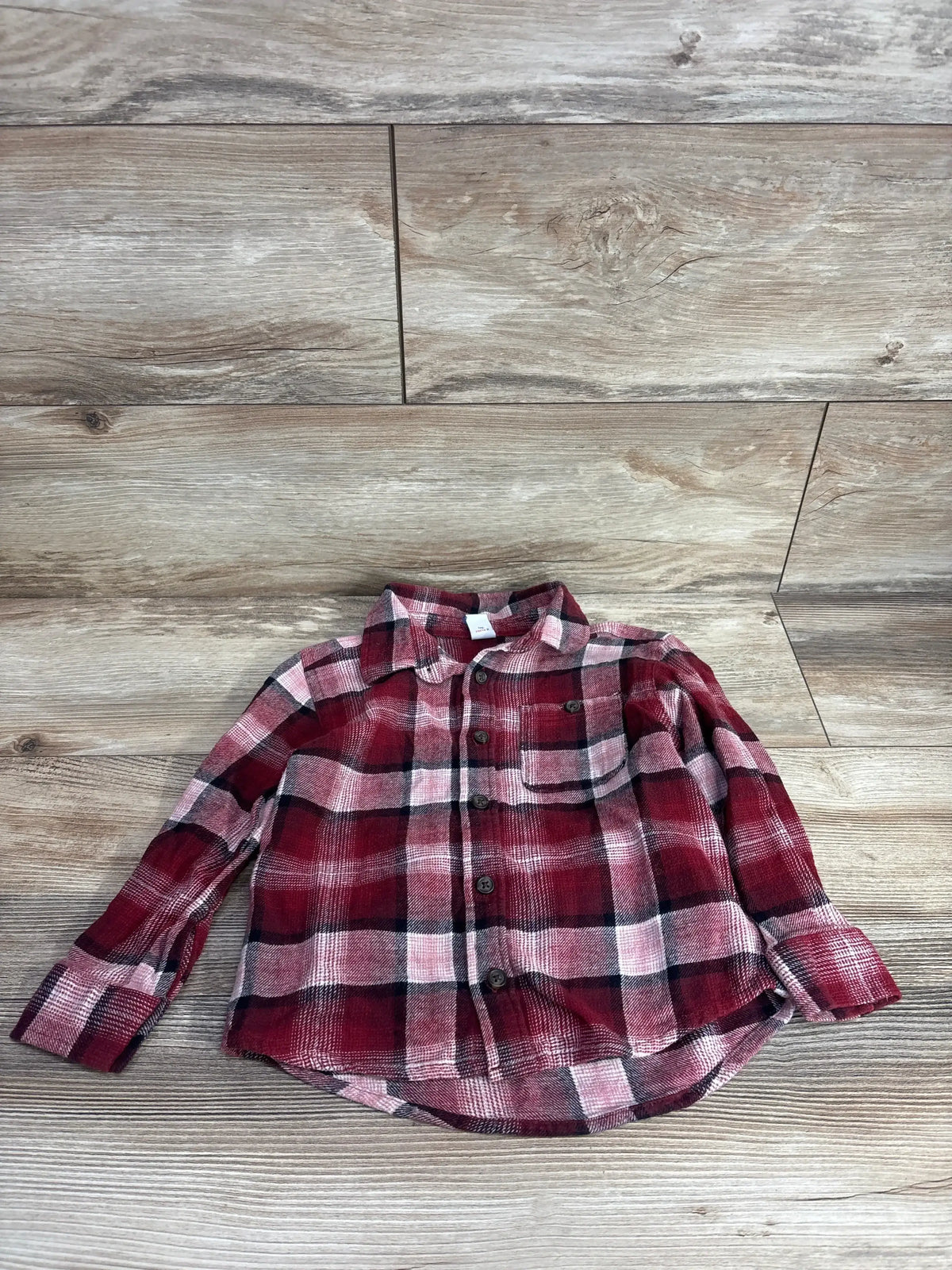 Red and black plaid long sleeve button-up toddler shirt on wooden background