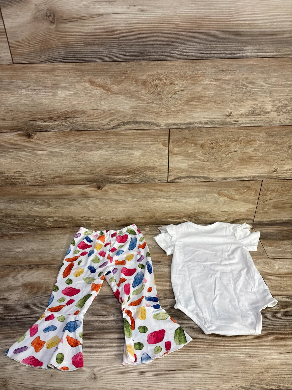Flat lay of 2pc set showcasing white short sleeve bodysuit and white flared pants with colorful watercolor dot print on wood plank floor